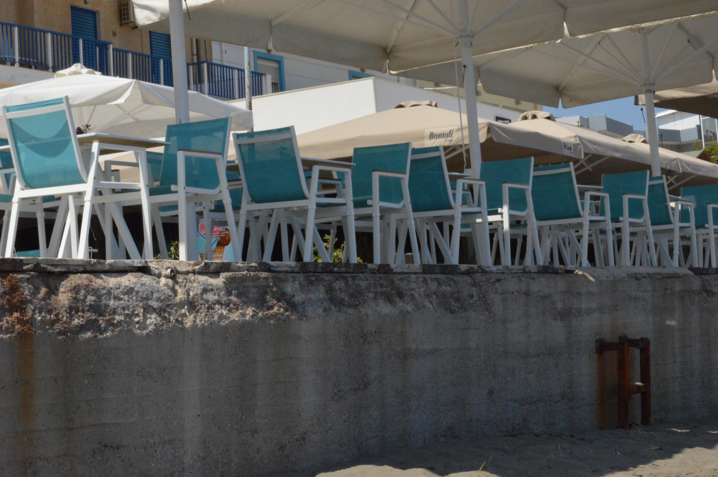 Empty patio with blue chairs and white umbrellas at a beachside restaurant or cafe.
