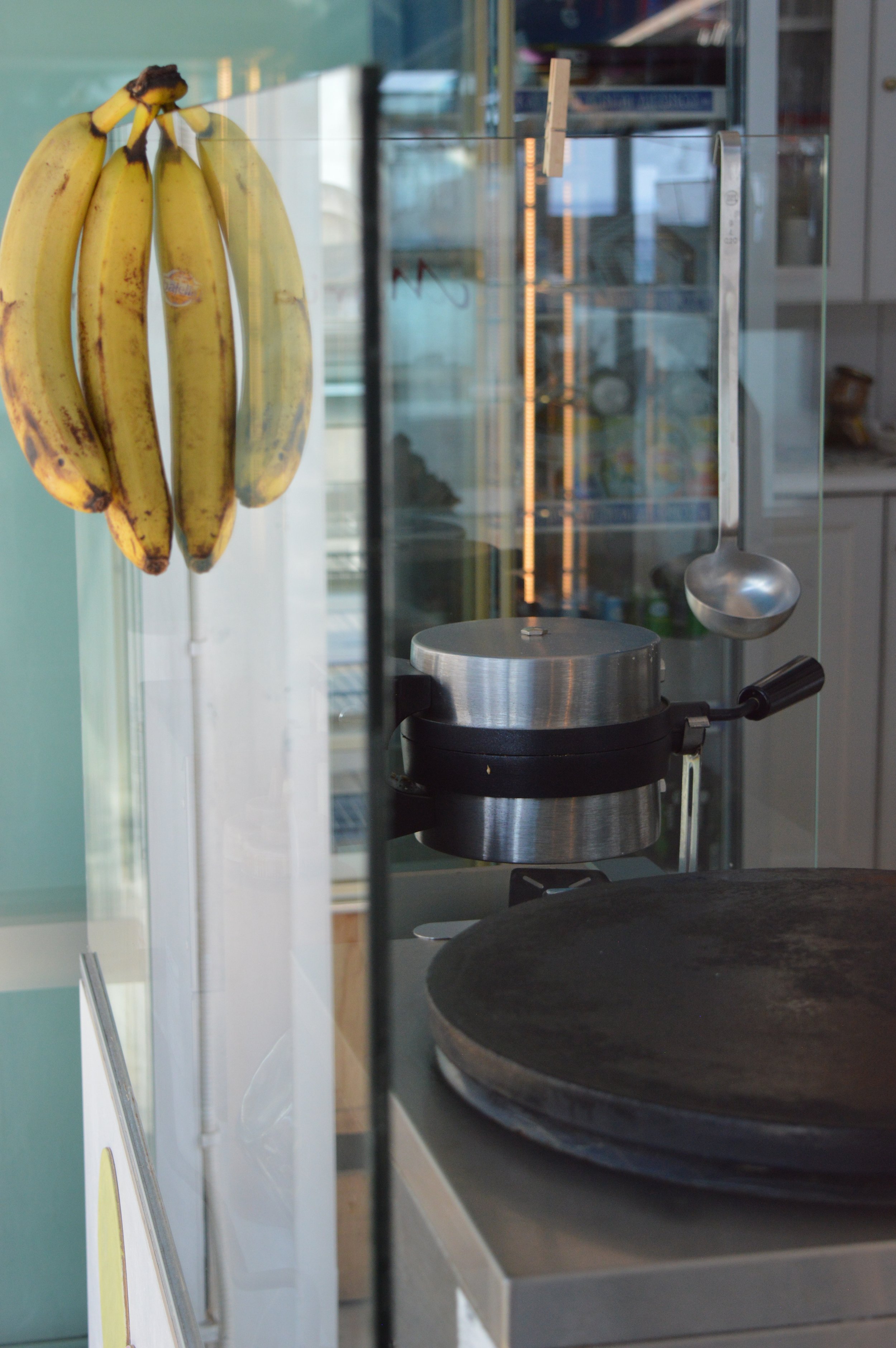 Gelateria Maria - A bunch of bananas hanging on a display, with a metal crepe maker and a ladle visible in the background.