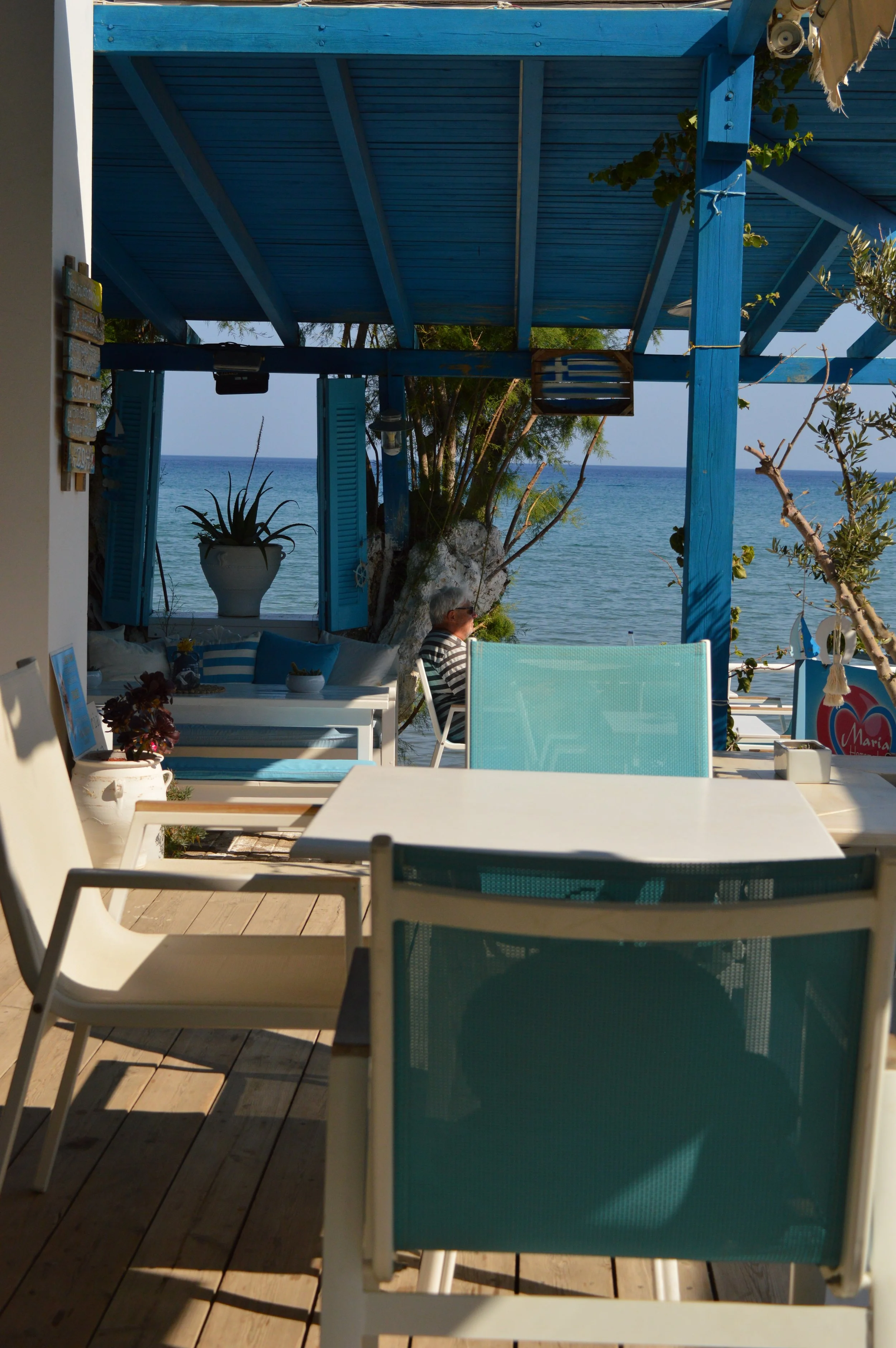 Outdoor seating area with chairs, table, and a view of the ocean, with a blue wooden pergola and some plants.