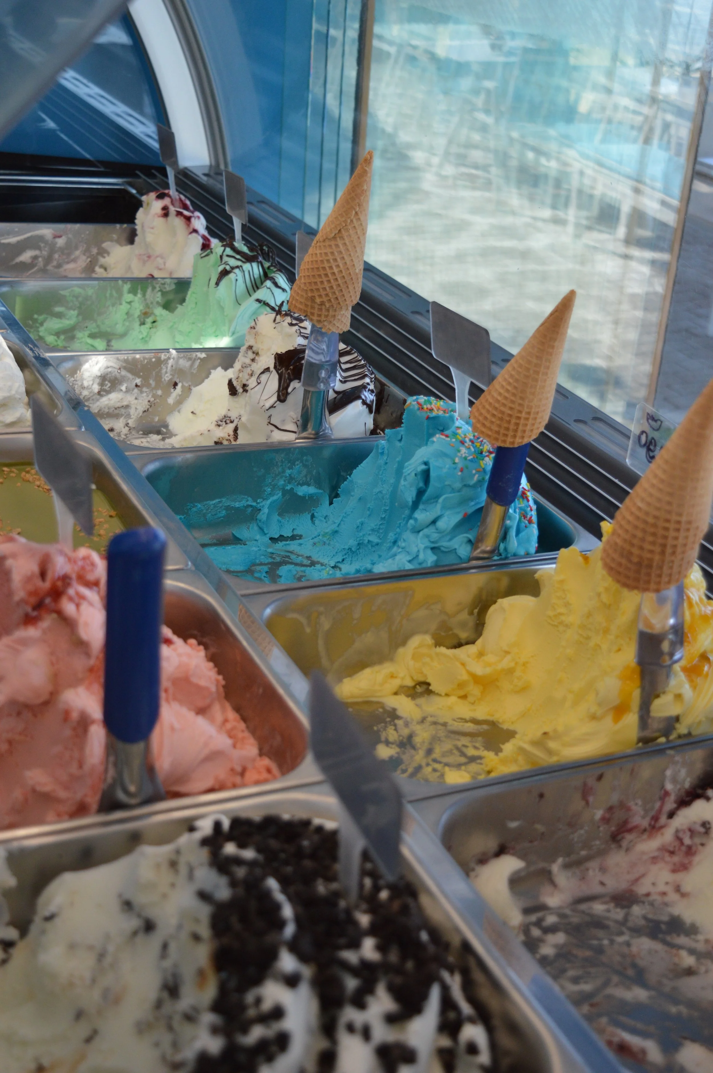 Gelateria Maria - Various flavors of ice cream in metal containers at an ice cream shop, with waffle cone scoops placed in some of the containers.
