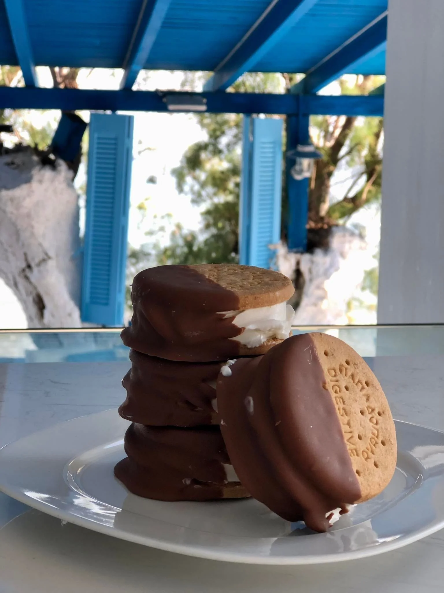 Stack of three chocolate-covered sandwich cookies with one cookie leaning against the stack, on a white plate.
