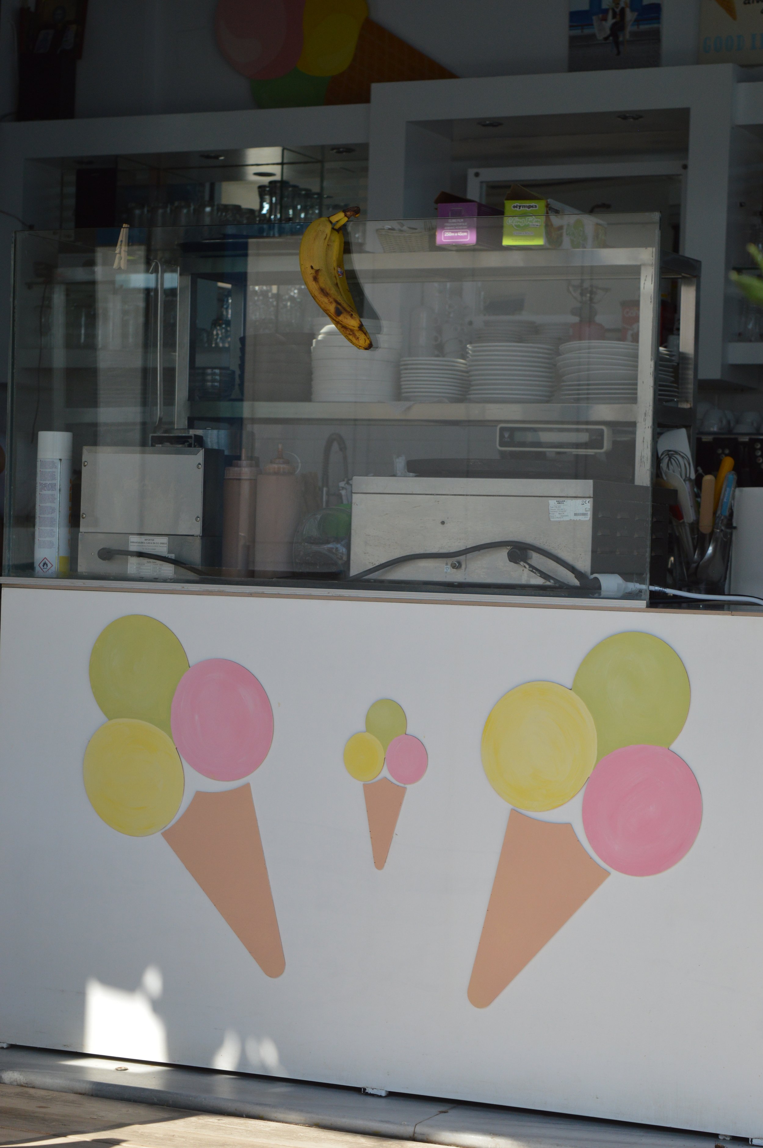 Gelateria Maria - Ice cream shop counter with a painted sign of three ice cream cones with pink and yellow scoops on the front.