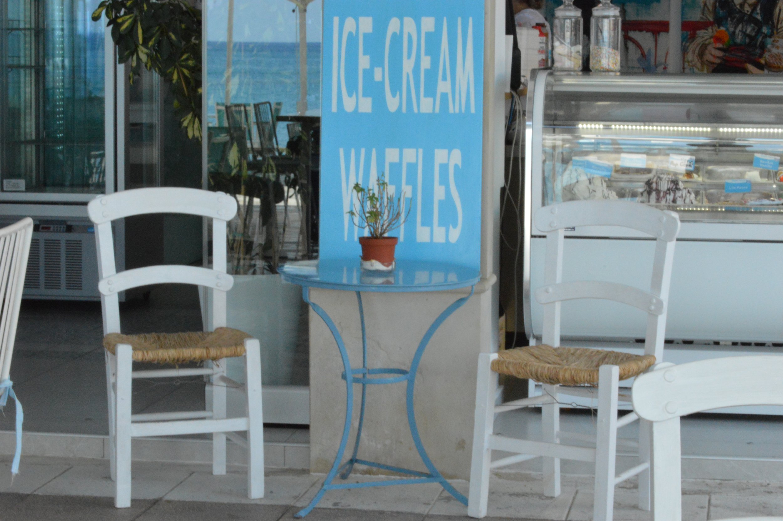 Gelateria Maria - Outdoor ice cream shop with white chairs, a small blue table, a sign that says 'Ice Cream Waffles', and a display case of ice cream