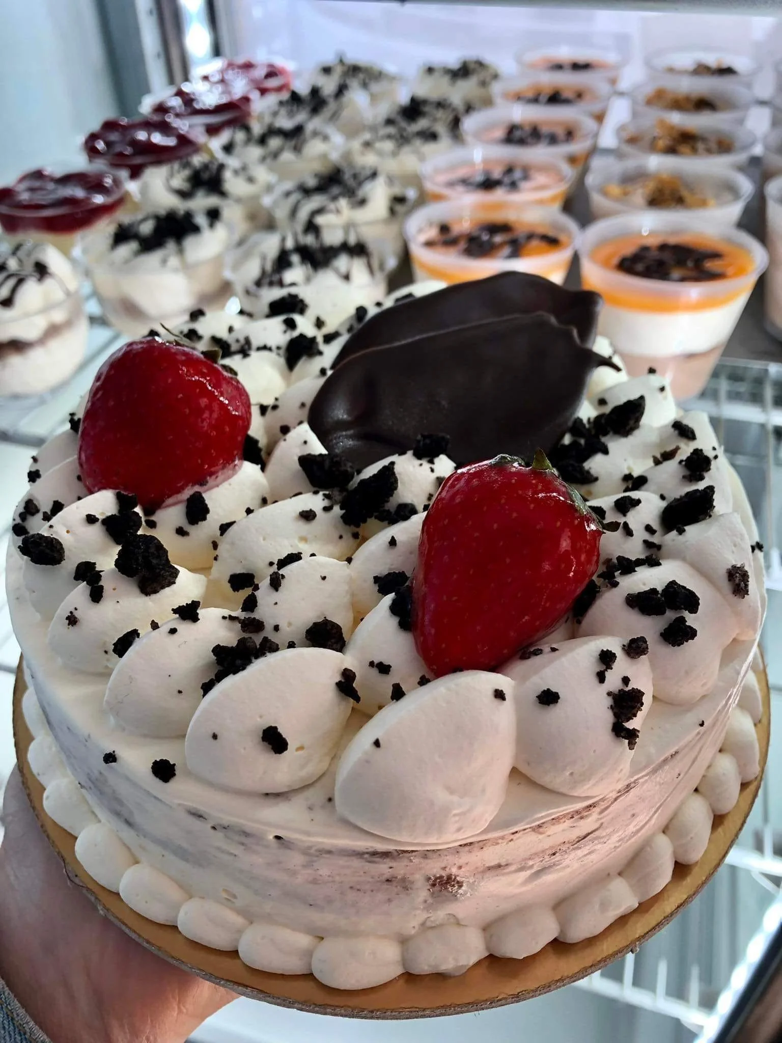 Gelateria Maria - A cake decorated with strawberries, chocolate, and cream, surrounded by small whipped cream dollops and cookie crumbs.