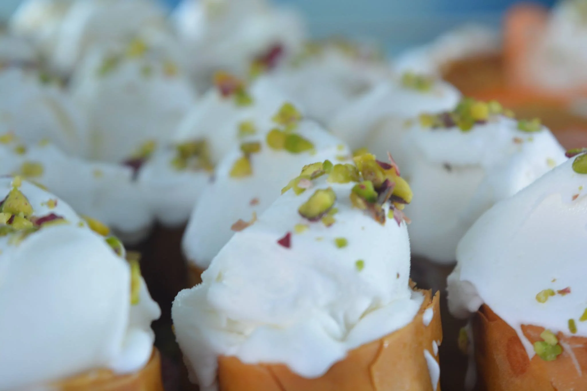 Gelateria Maria - Close-up of three ice cream cones with white soft serve topped with chopped pistachios.