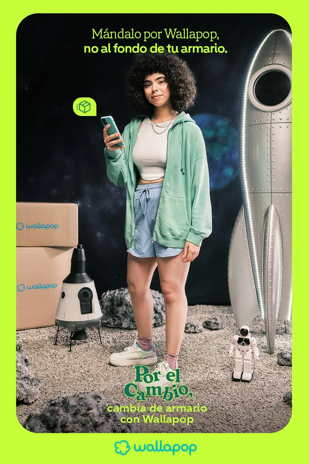 A woman standing in a space-themed setting, wearing casual clothes and holding a smartphone, with a rocket, a small robot, and a cardboard box in the background, promoting Wallapop for swapping items.