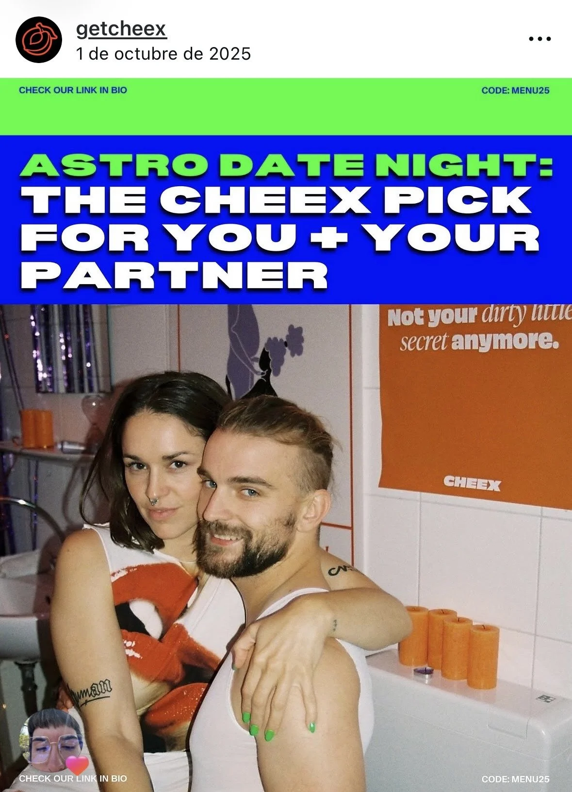 A woman and a man are sitting close together, smiling at the camera in a room with white tiled walls and orange-colored items. The woman has dark hair, a septum piercing, and green nail polish, while the man has a beard and hairstyle. The background 
