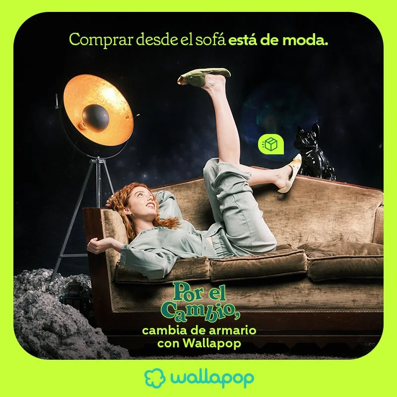 A woman lying on a vintage sofa, with one leg raised and bent over her head, in a surreal space-themed setting. There is a black dog-shaped object on the right and a large vintage-style lamp on the left. Text in Spanish promotes buying furniture on sale with Wallapop.