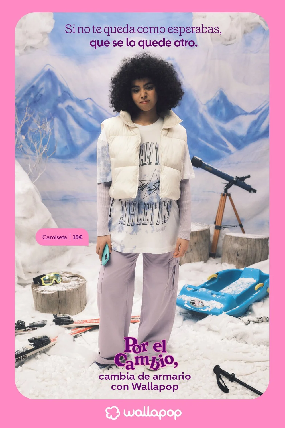 A girl standing in a winter-themed backdrop with snow, mountains, and a telescope. She is wearing a puffy vest, a tie-dye t-shirt, and light-colored pants, holding a smartphone. Ski equipment and snow accessories are on the ground. The image has Spanish text promoting a change with Wallapop.