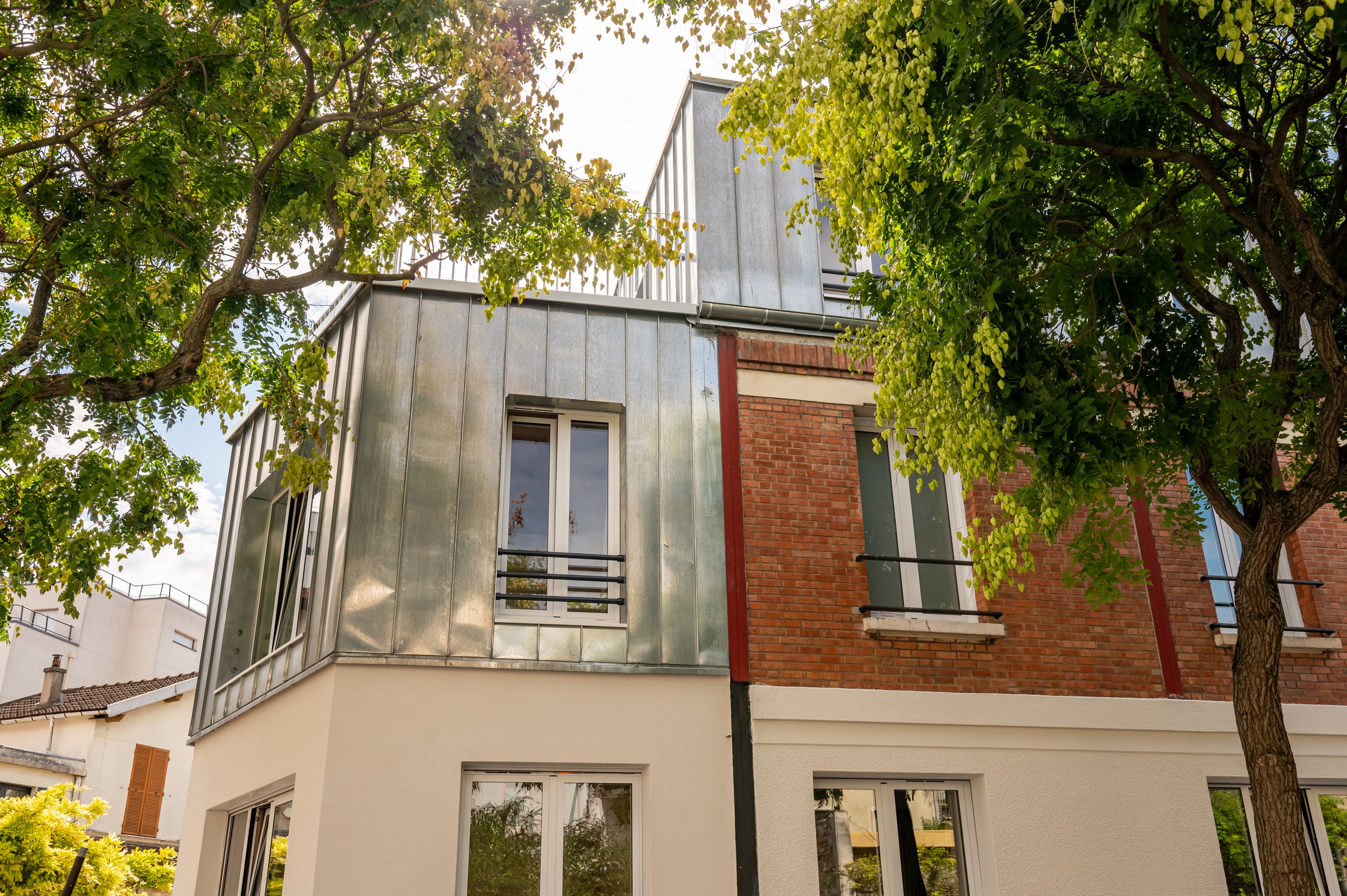 Façade d'un immeuble résidentiel avec fenêtres, en partie cachée par des arbres aux feuilles vertes.