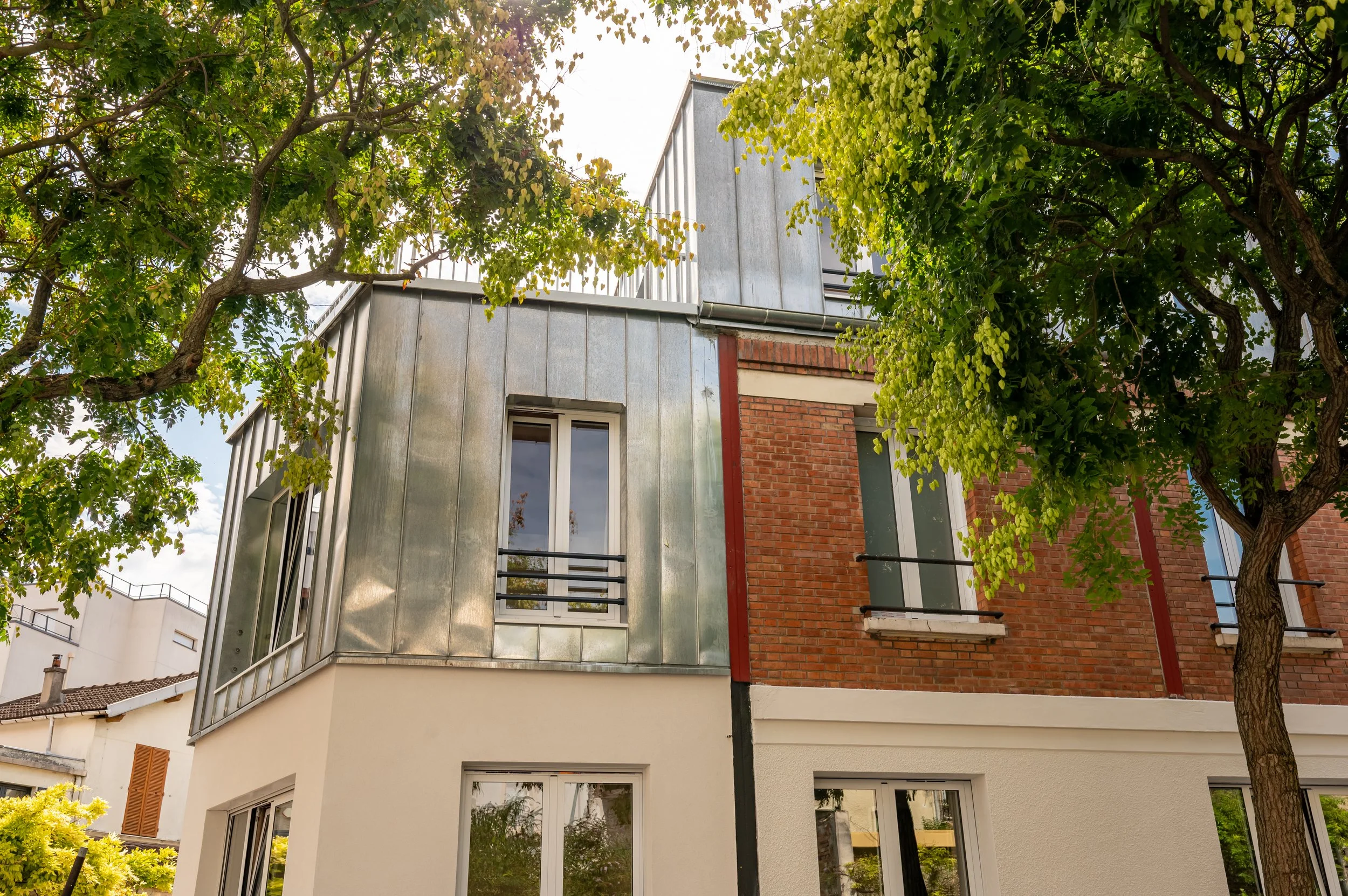 Bâtiment moderne avec des murs en briques rouges et en métal, entouré d'arbres feuillus verts.