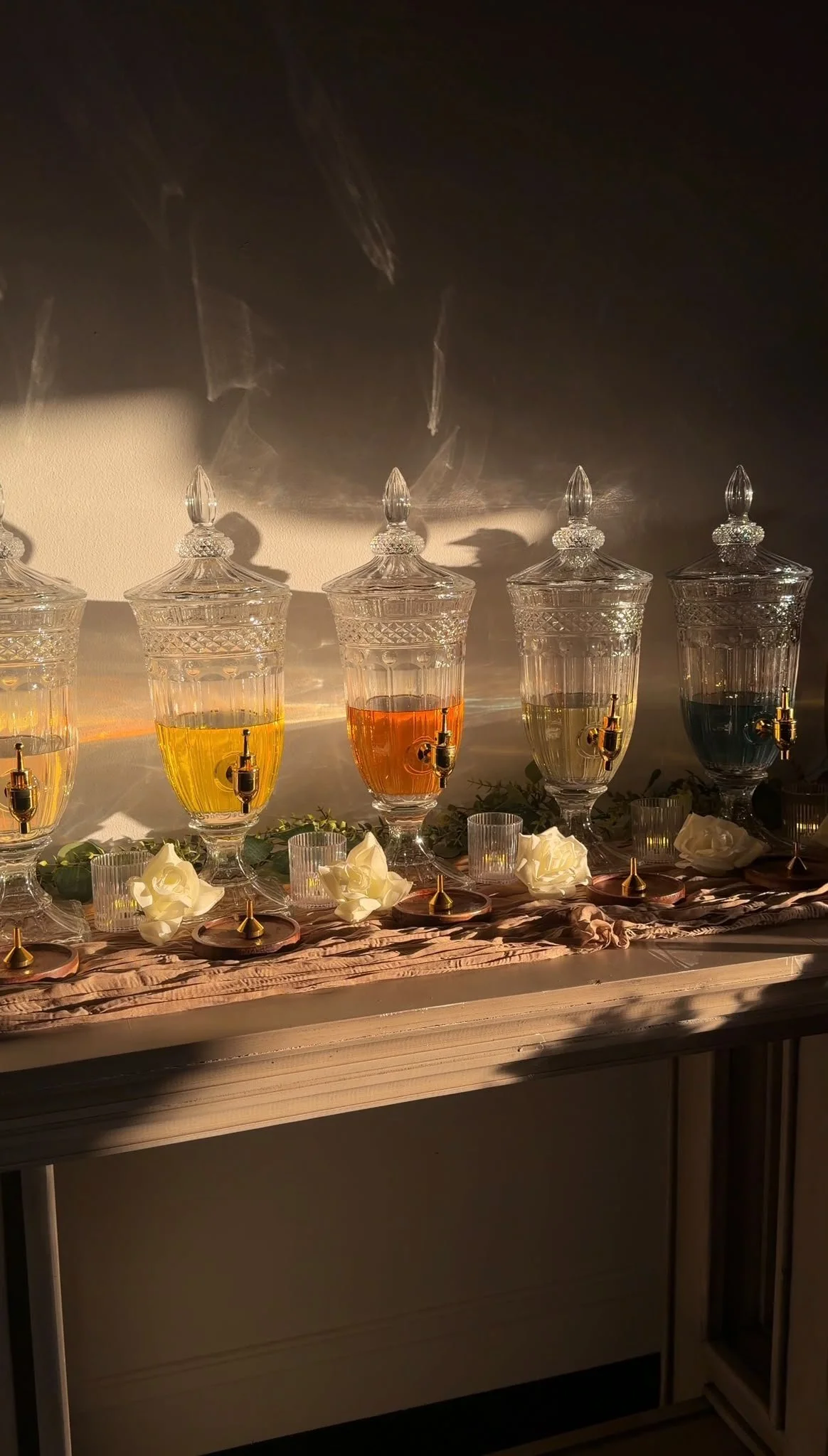 Decorative glass jars with colored liquids, arranged on a table with flowers and candles for a celebration or party.