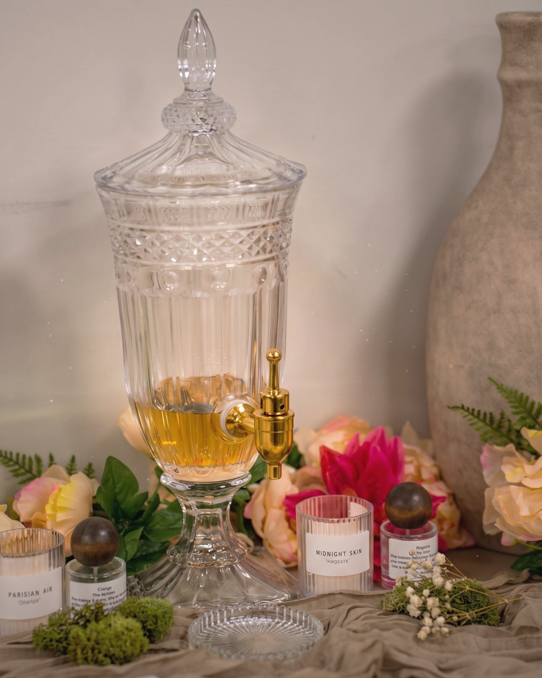 A decorative glass perfume bottle with a crystal lid, placed among floral arrangements and scented candles on a soft fabric surface.