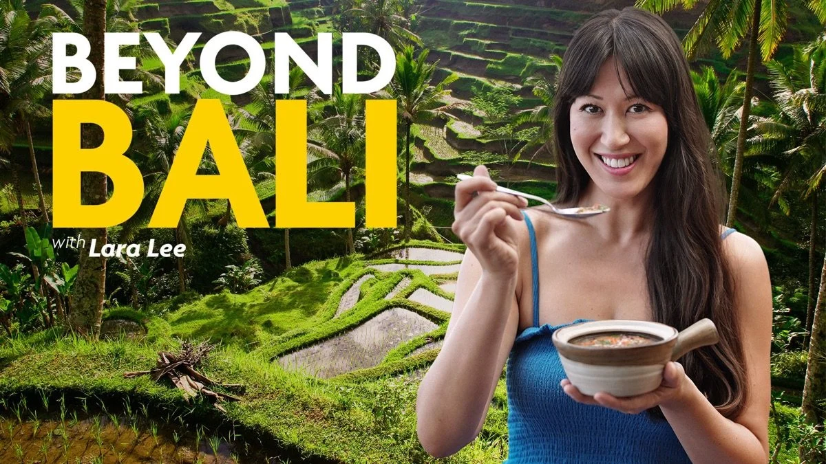 A woman with long dark hair, wearing a blue tank top, smiling and holding a spoon and a bowl of food, standing in front of a lush green terraced rice field with palm trees, with the text "BEYOND BALI with Lara Lee" on the image.