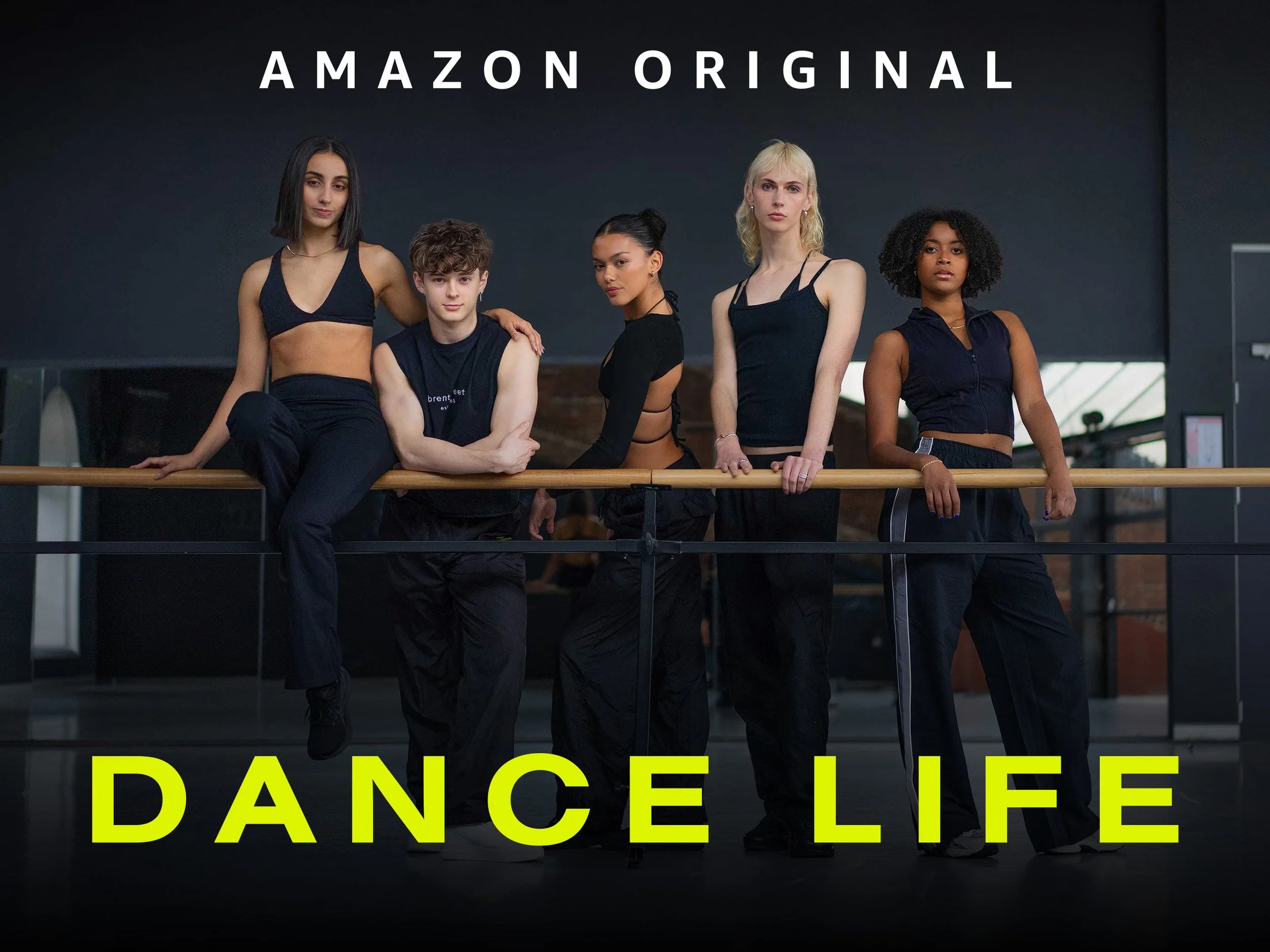 Group of five diverse young female dancers standing together in dance studio, wearing dance activewear, with a ballet barre in front of them, and the words 'Amazon Original' at the top and 'DANCE LIFE' at the bottom.