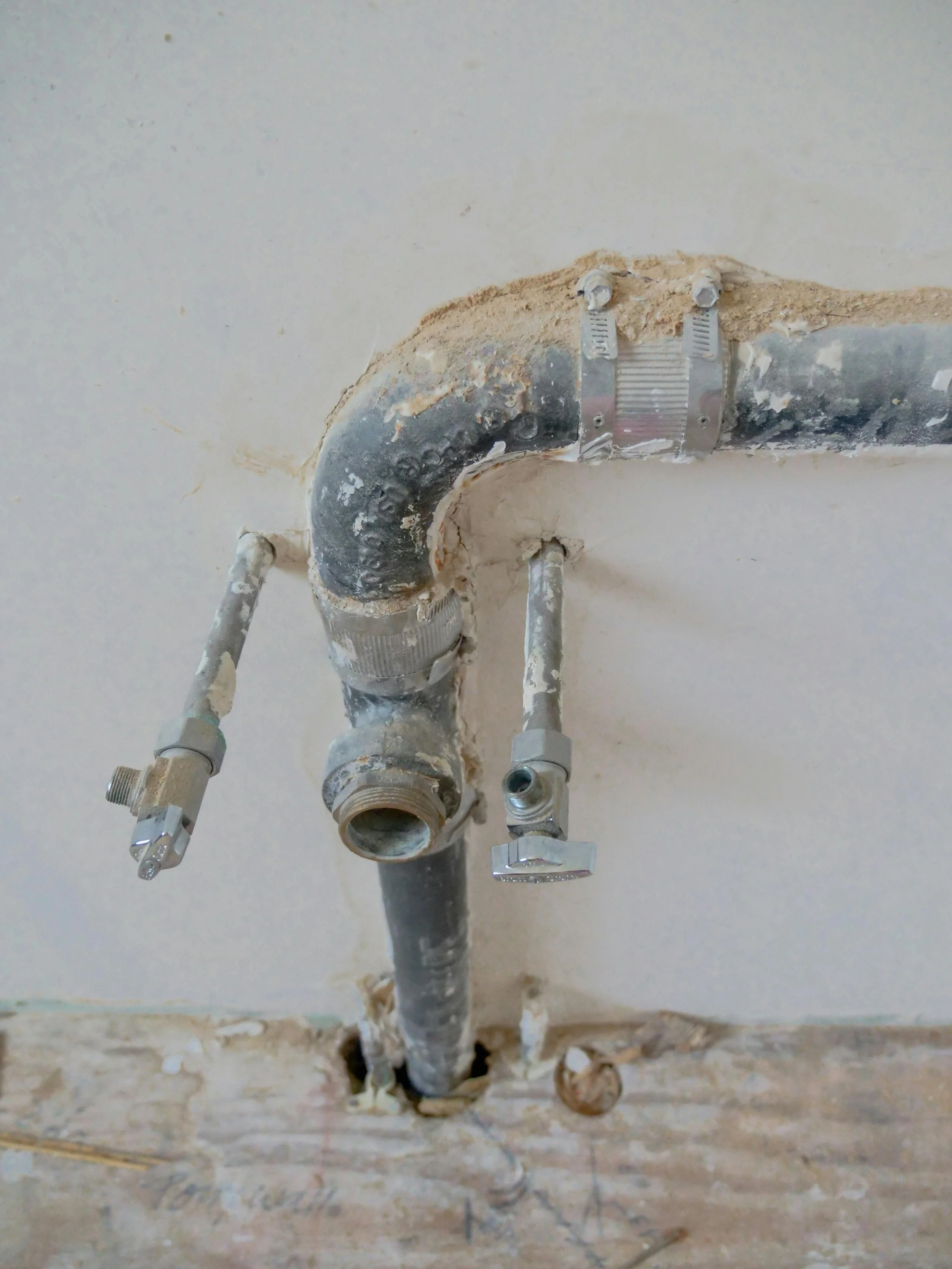Tubi e raccordi di metallo installati nel soffitto di un edificio, con tracce di malta e cemento circostante, probabilmente per impianti idraulici.
