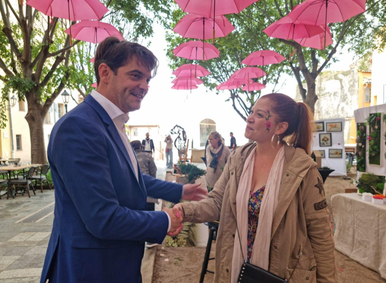 Deux personnes se serrent la main sous des parapluies roses suspendus, échanges amicaux lors d'un événement en plein air.