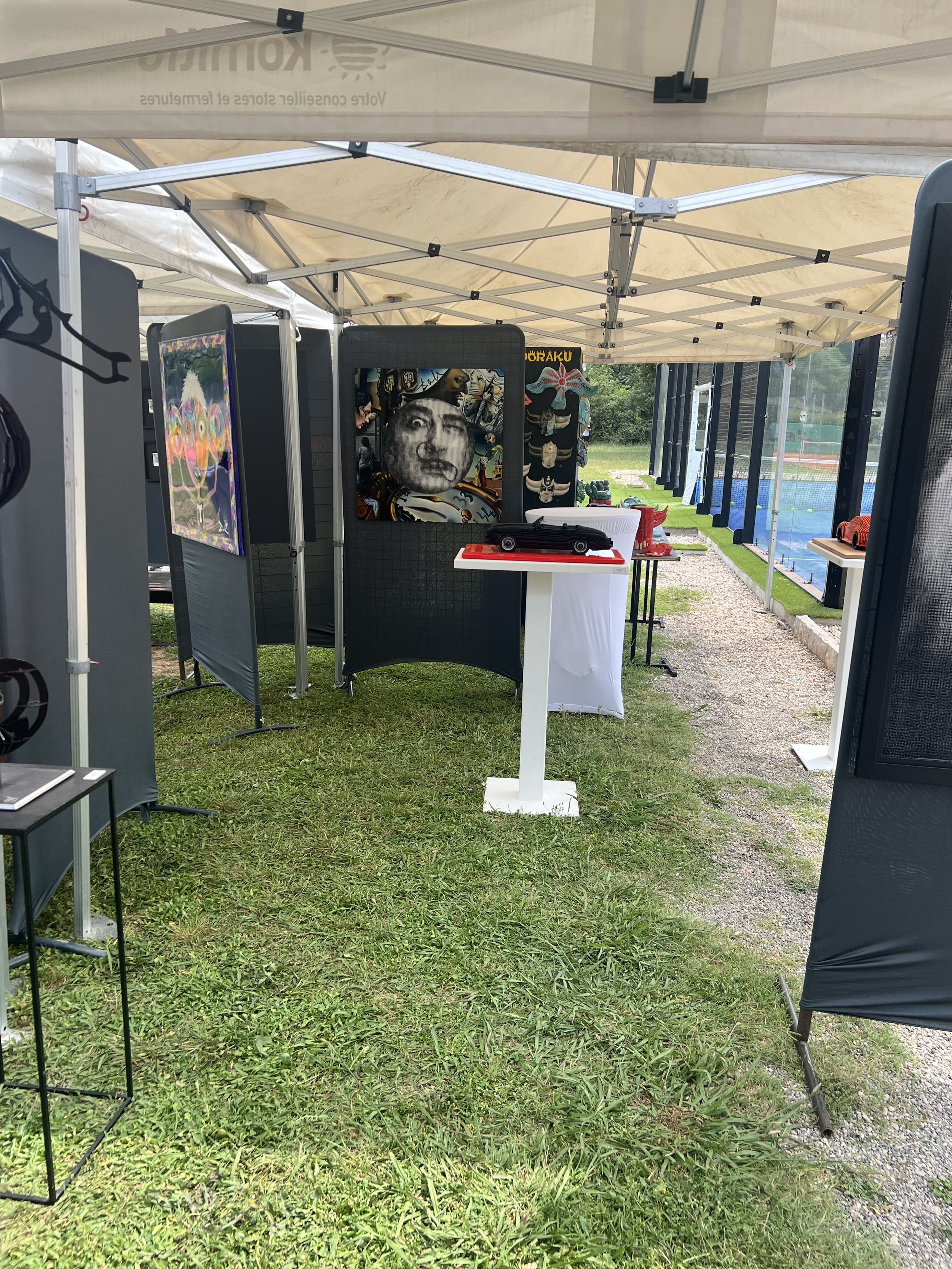 Stand d'exposition en plein air avec des panneaux d'affichage, des produits et des décorations, ainsi qu'une piscine en arrière-plan.
