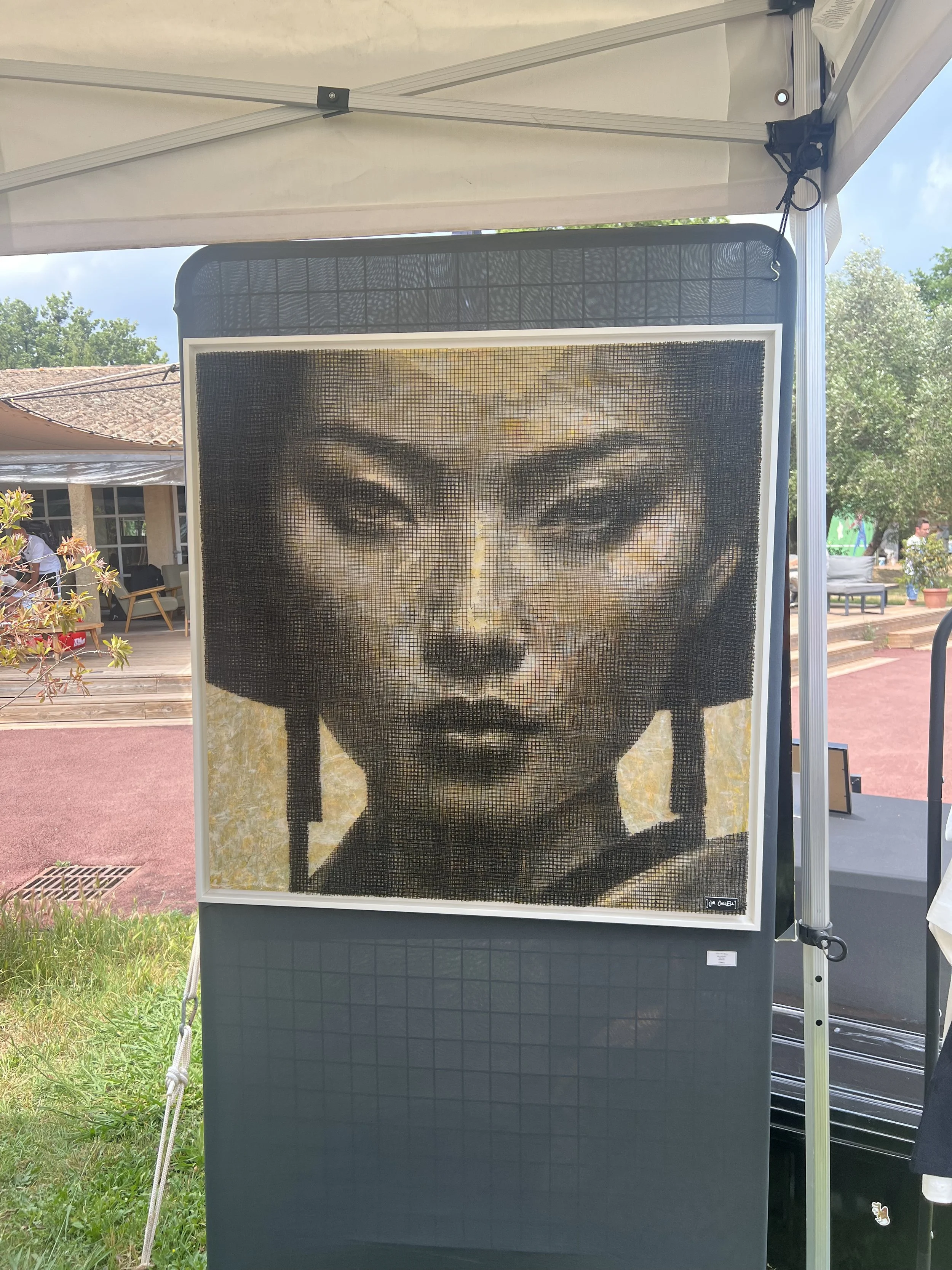Une œuvre d'art représentant un visage féminin, probablement une sculpture ou un tableau, sous forme de mosaïque ou de pixel art, exposée à l'extérieur lors d'un événement en plein air.