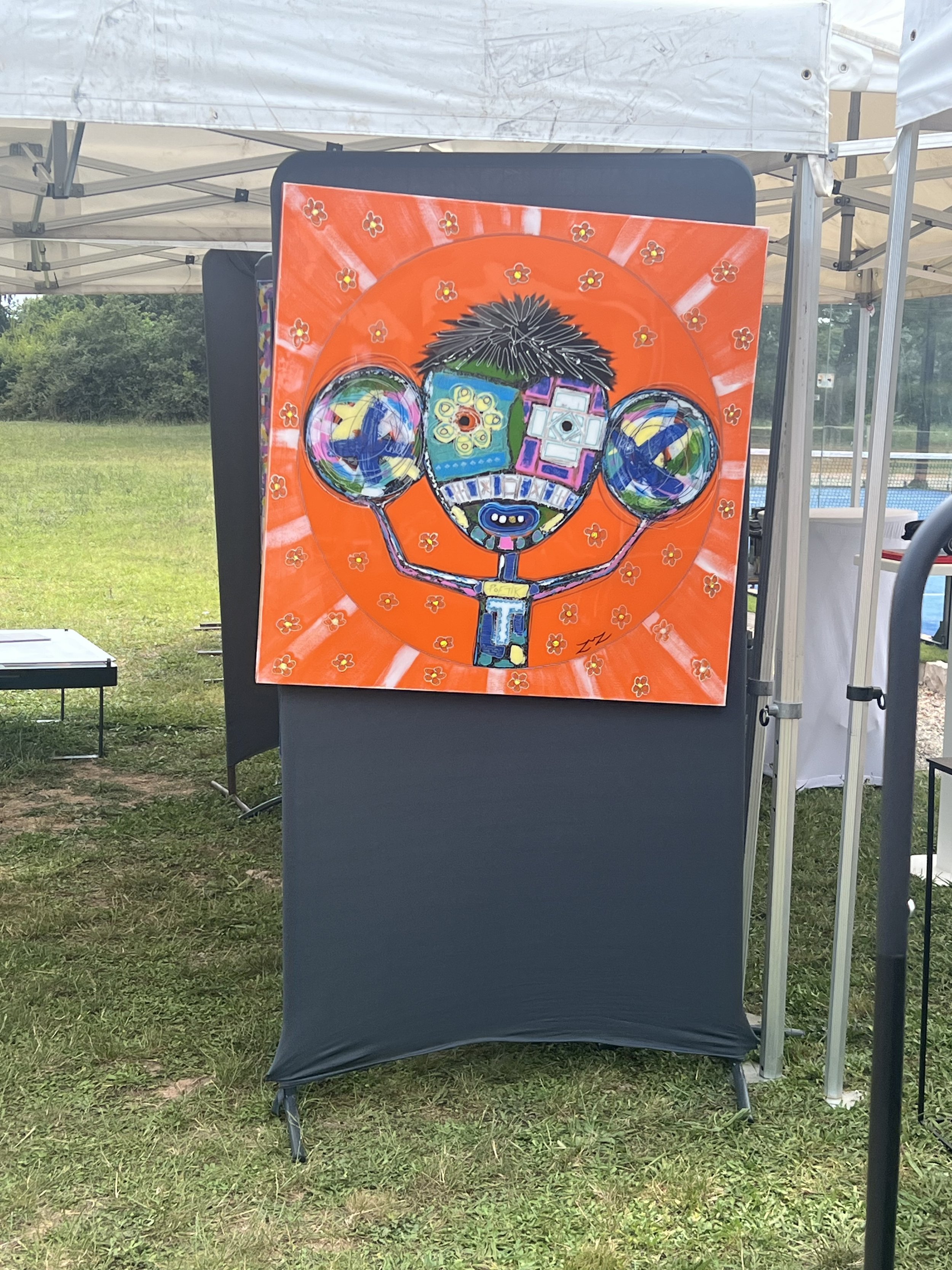 Une peinture artistique représentant un personnage avec une tête en forme de visage composé de formes géométriques de différentes couleurs, entouré d'un fond orange avec de petites fleurs rouges. Le personnage a deux bras levés sur les côtés, tenant chacun une sphère colorée.
