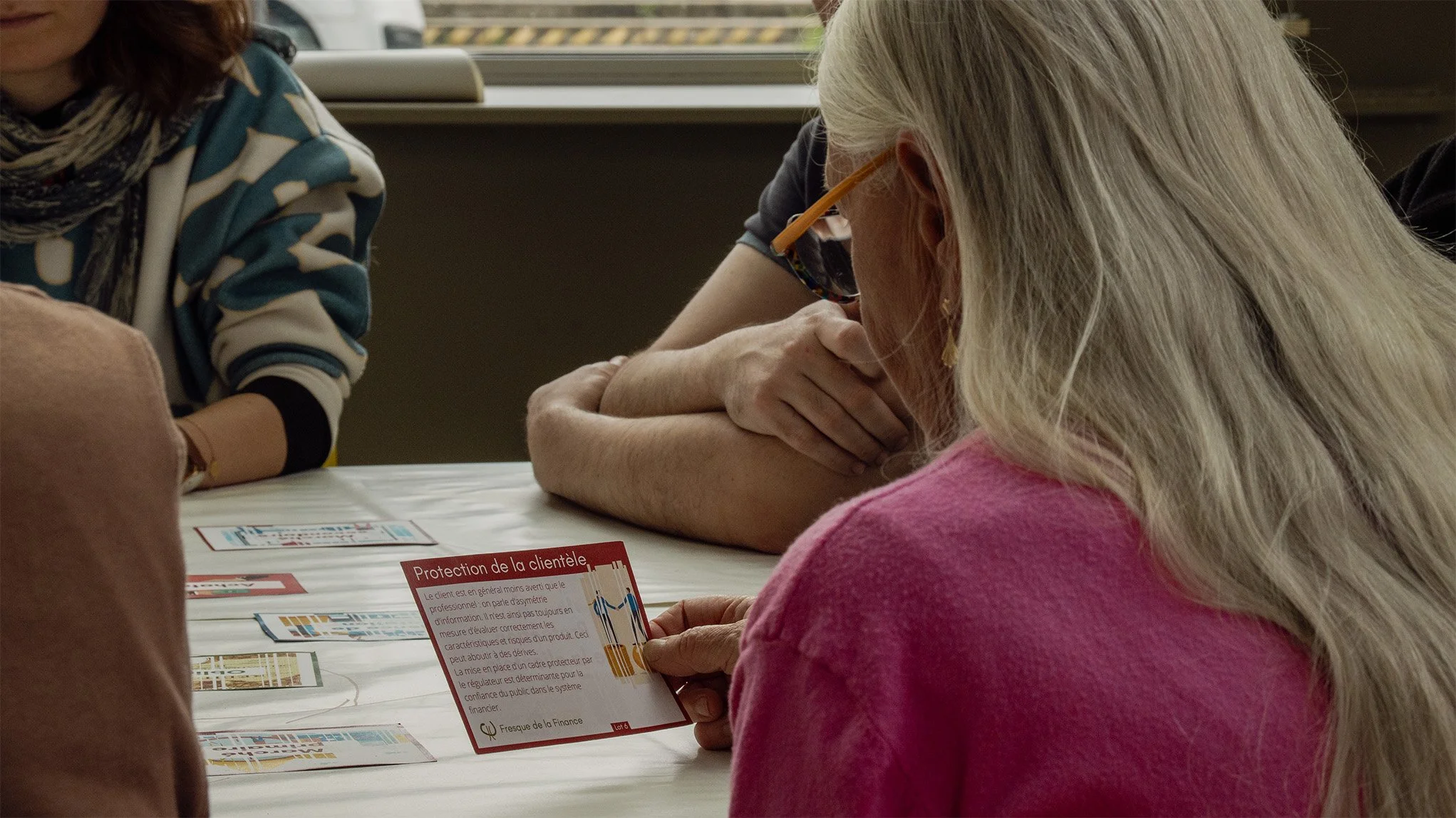 Une femme âgée avec des cheveux gris et portant des lunettes orange regarde une carte de la fresque sur une table avec une autre personne.