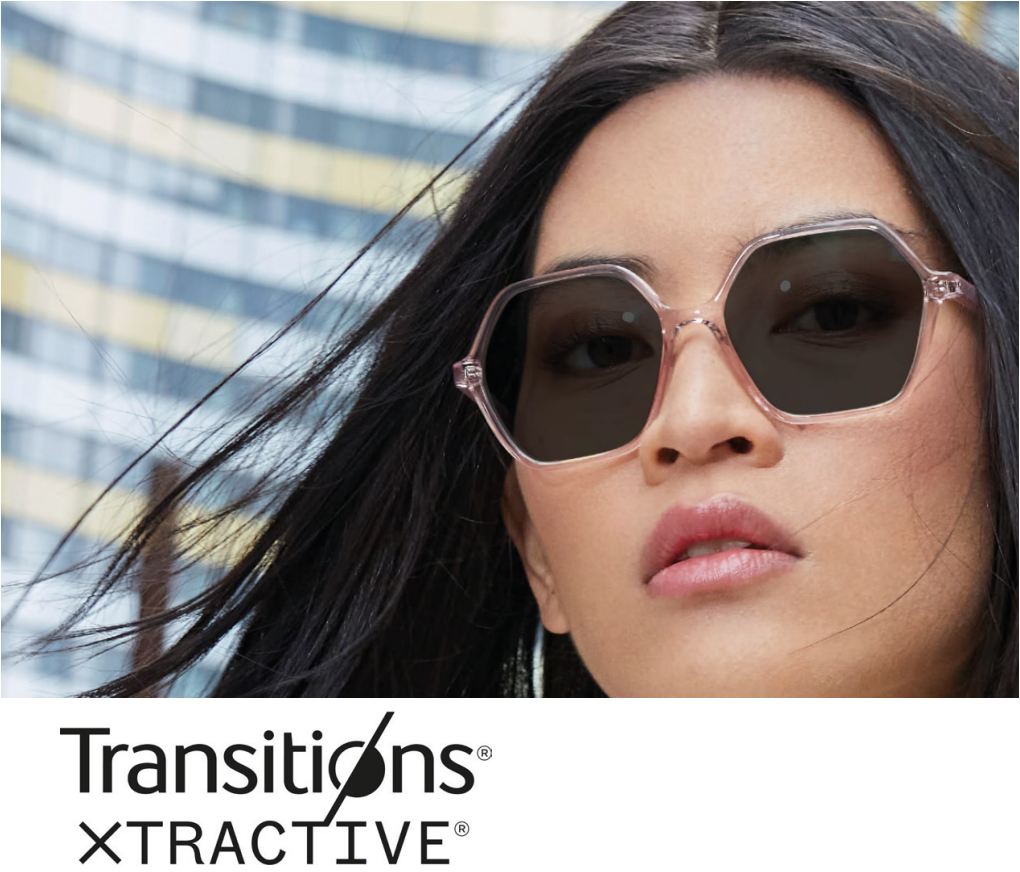 A woman with long black hair wearing pink sunglasses and a serious expression, with modern buildings in the background.