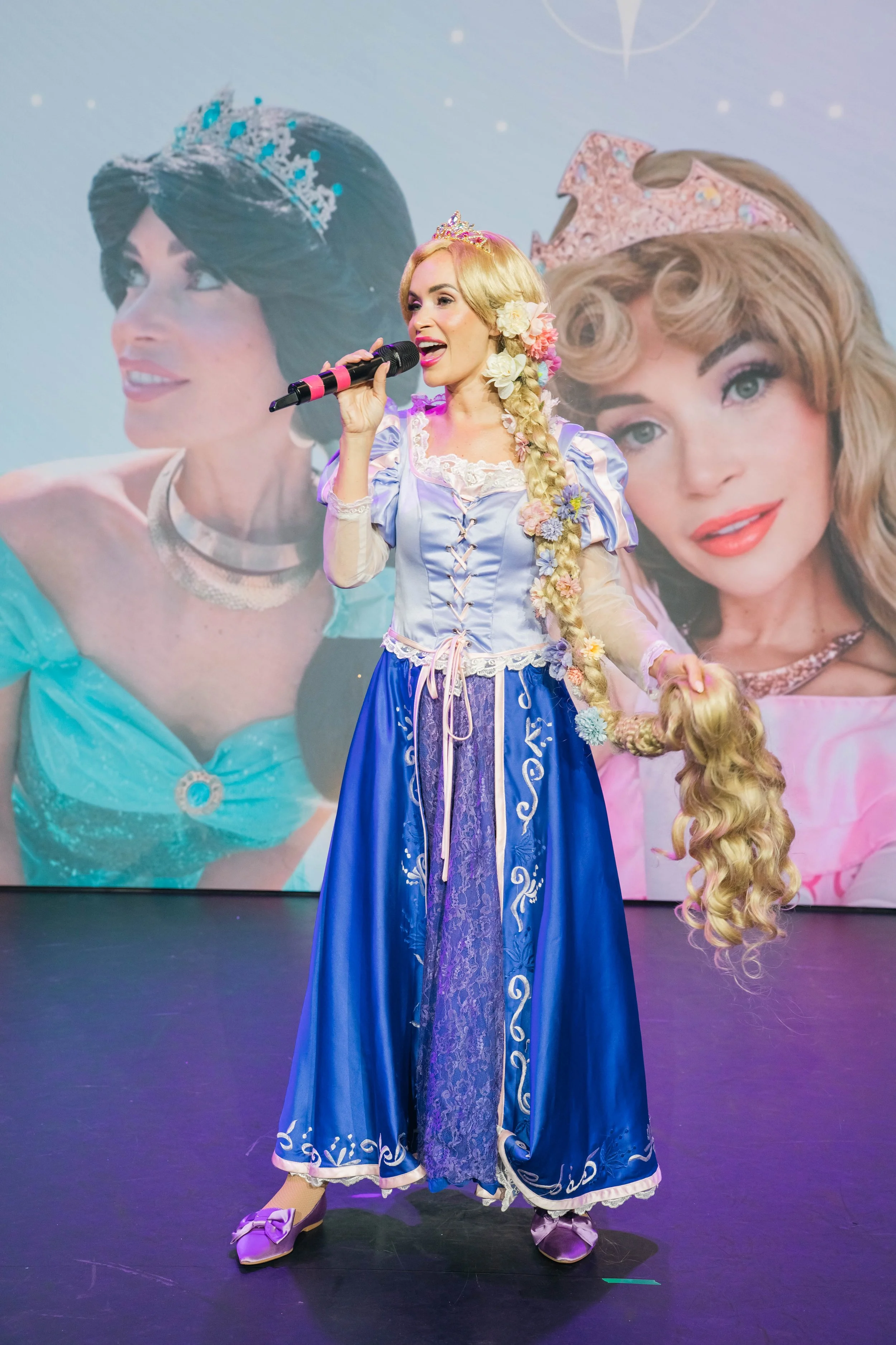 Person dressed as Rapunzel from Disney's Tangled singing into a microphone on stage, with a large backdrop featuring images of Rapunzel in different poses.