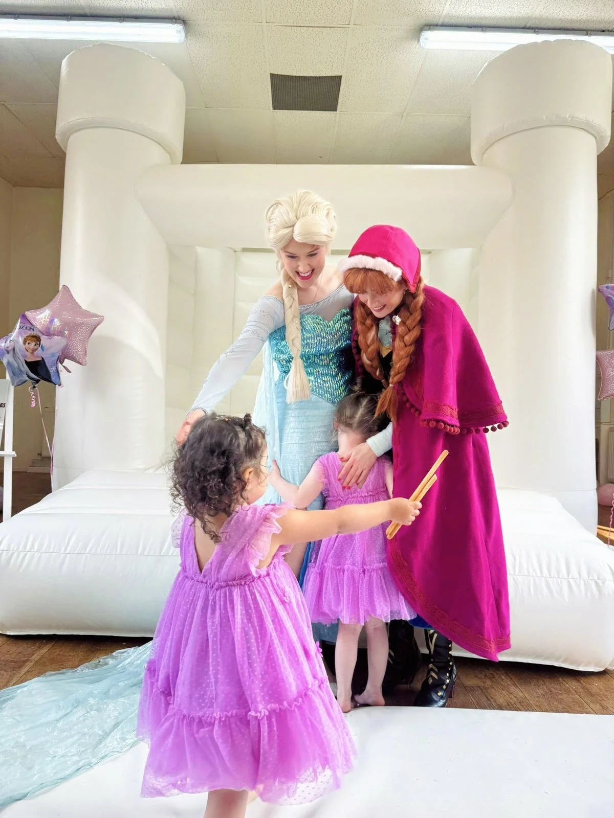 Children dressed as princesses and costumed characters, Elsa and Anna from Frozen, on an inflatable castle during a celebration.