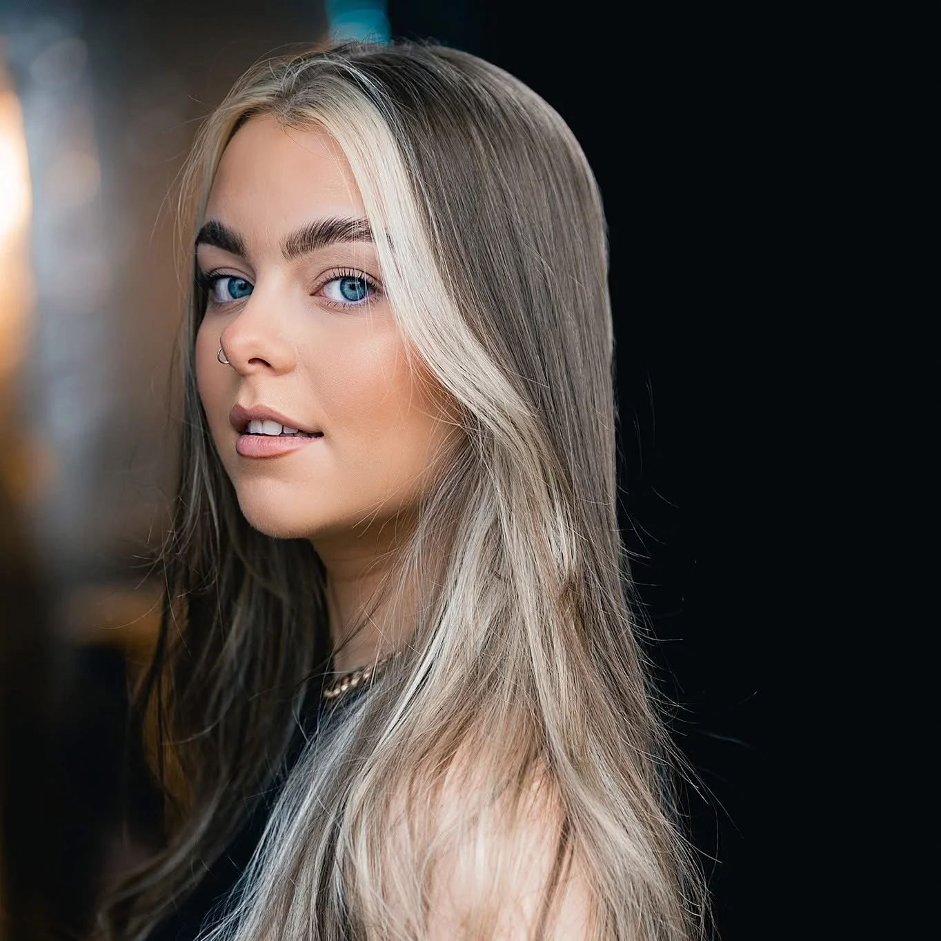 Close-up portrait of a young woman with long, blonde hair and bright blue eyes, against a black background.