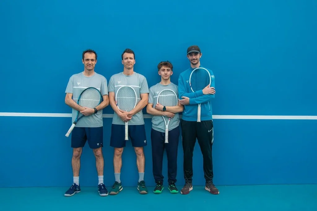 Quatre hommes debout avec des raquettes de tennis contre un mur bleu