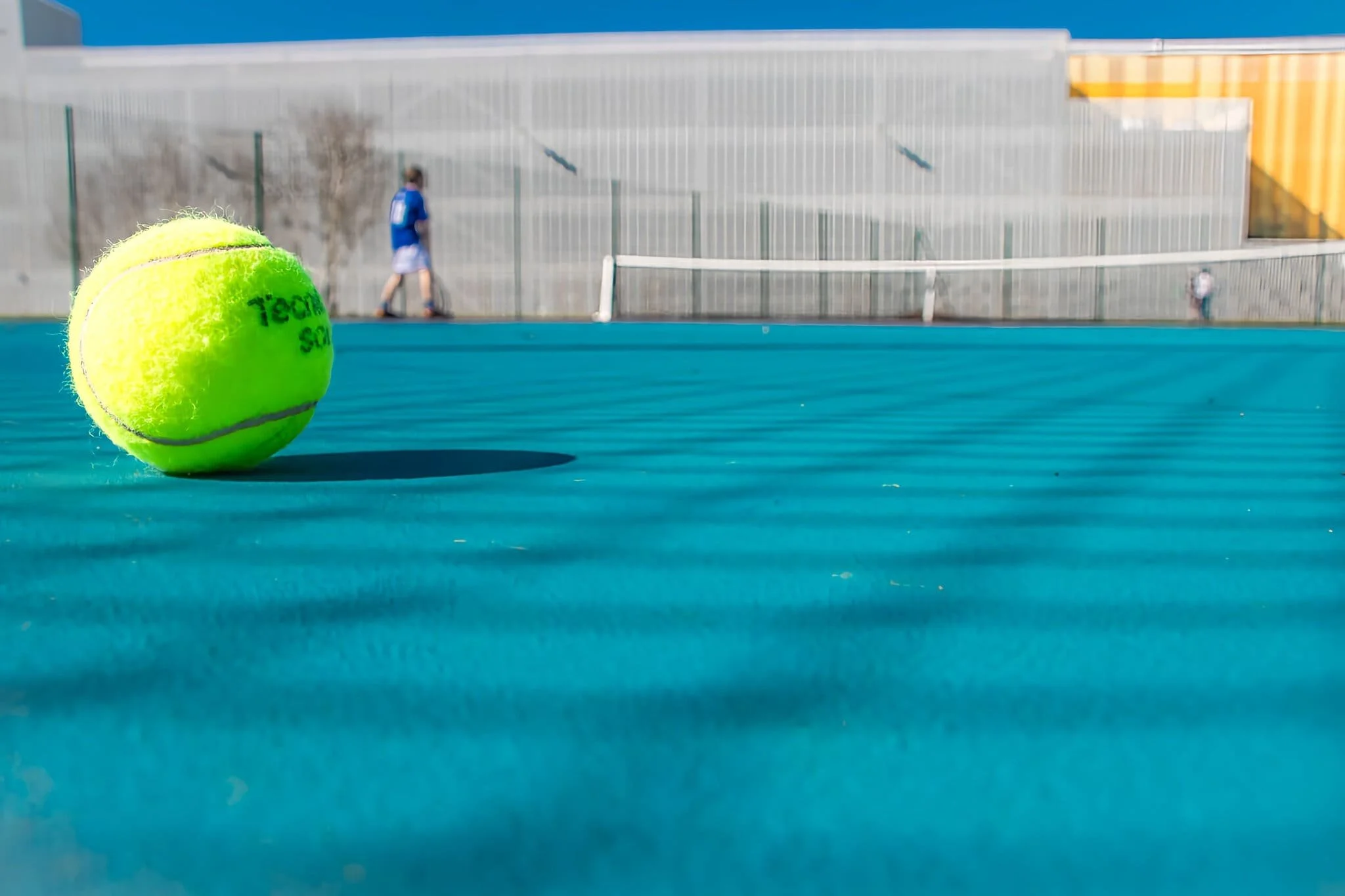 Une balle de tennis jaune sur un court de tennis bleu, avec deux joueurs en arrière-plan.