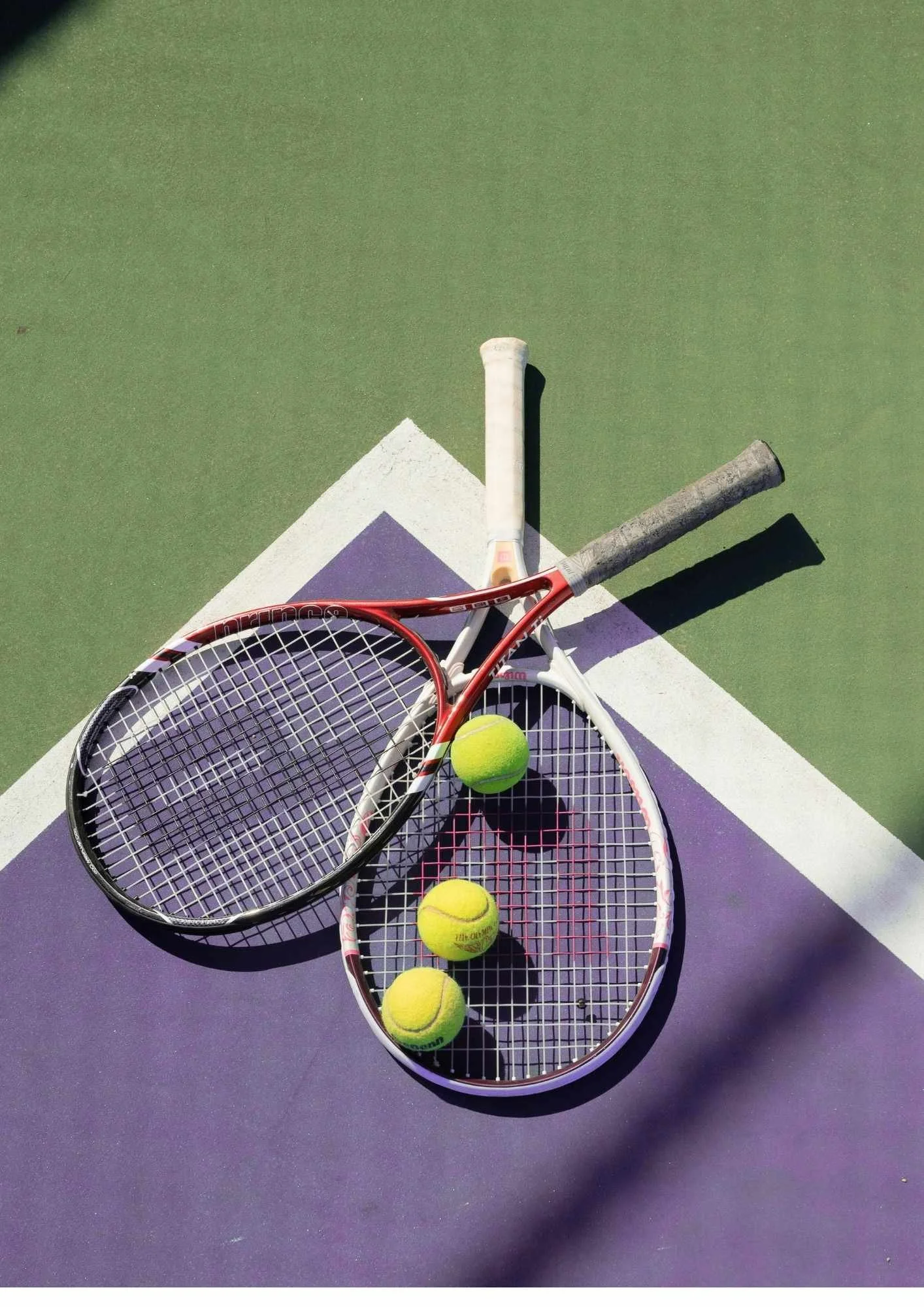 Deux raquettes de tennis avec quatre balles de tennis jaunes sur un terrain de tennis violet et vert.