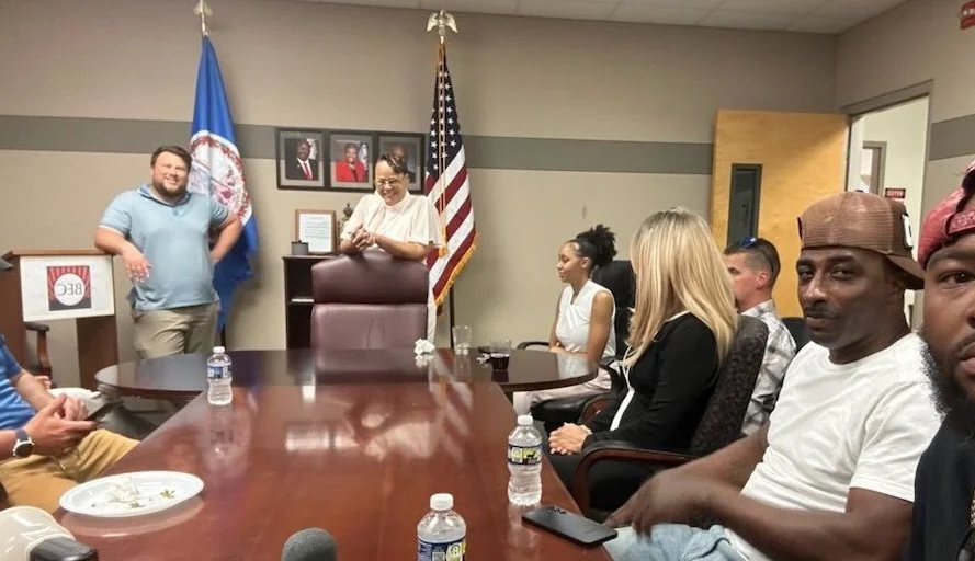 A group of people seated around a conference table in a room with American and organizational flags, photographs, and plaques on the wall.