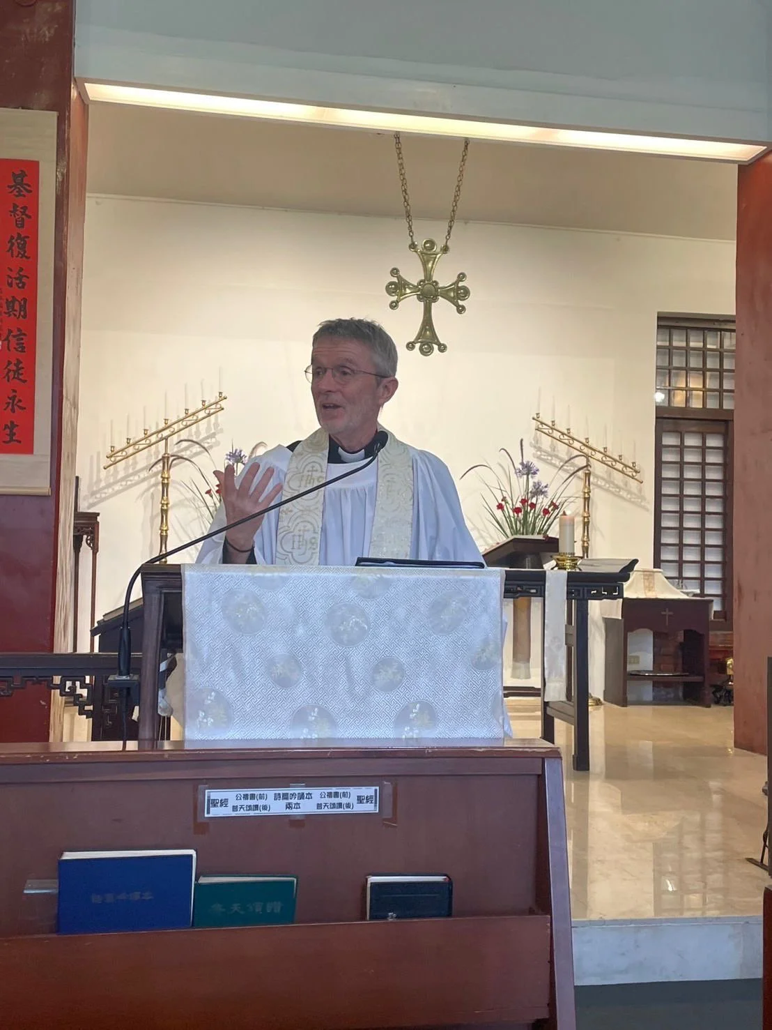 A priest standing at a lectern delivering a speech inside a church, with religious decorations and candles in the background.