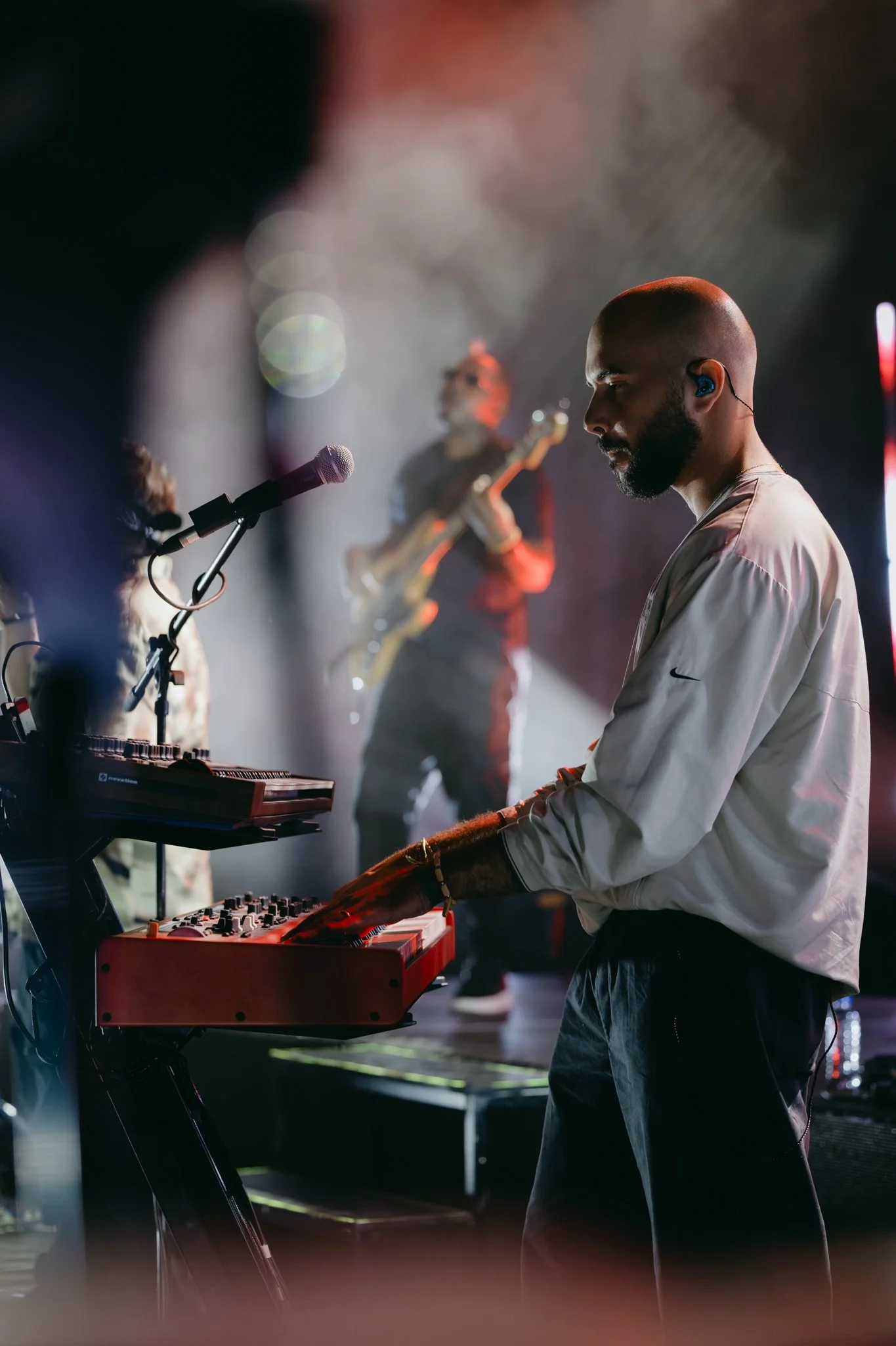 A piano player playing a keyboard on a live stage with musicians and a band