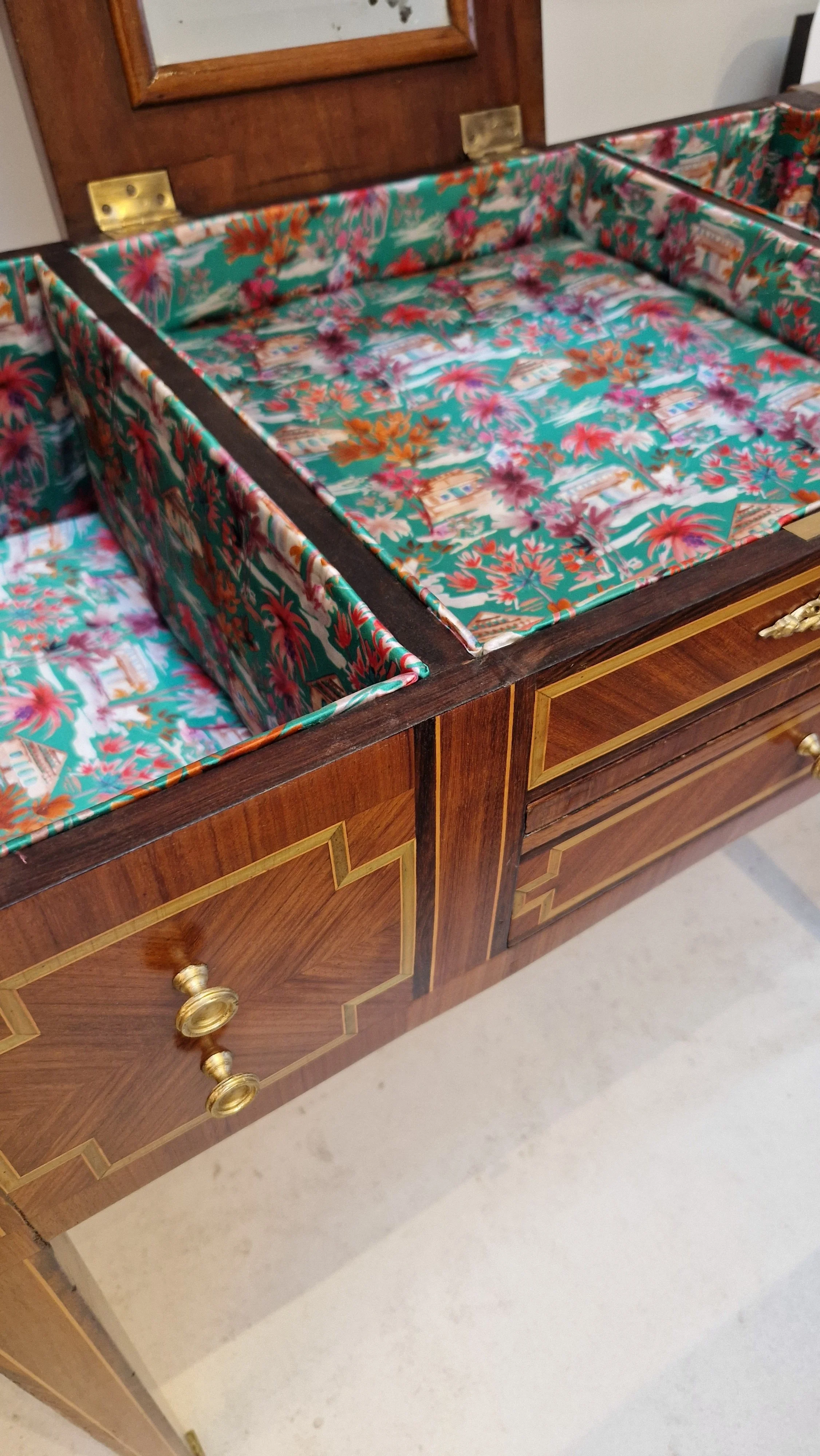 Une commode en bois avec un tissu décoratif à l'intérieur, comportant des tiroirs avec des poignées en or.