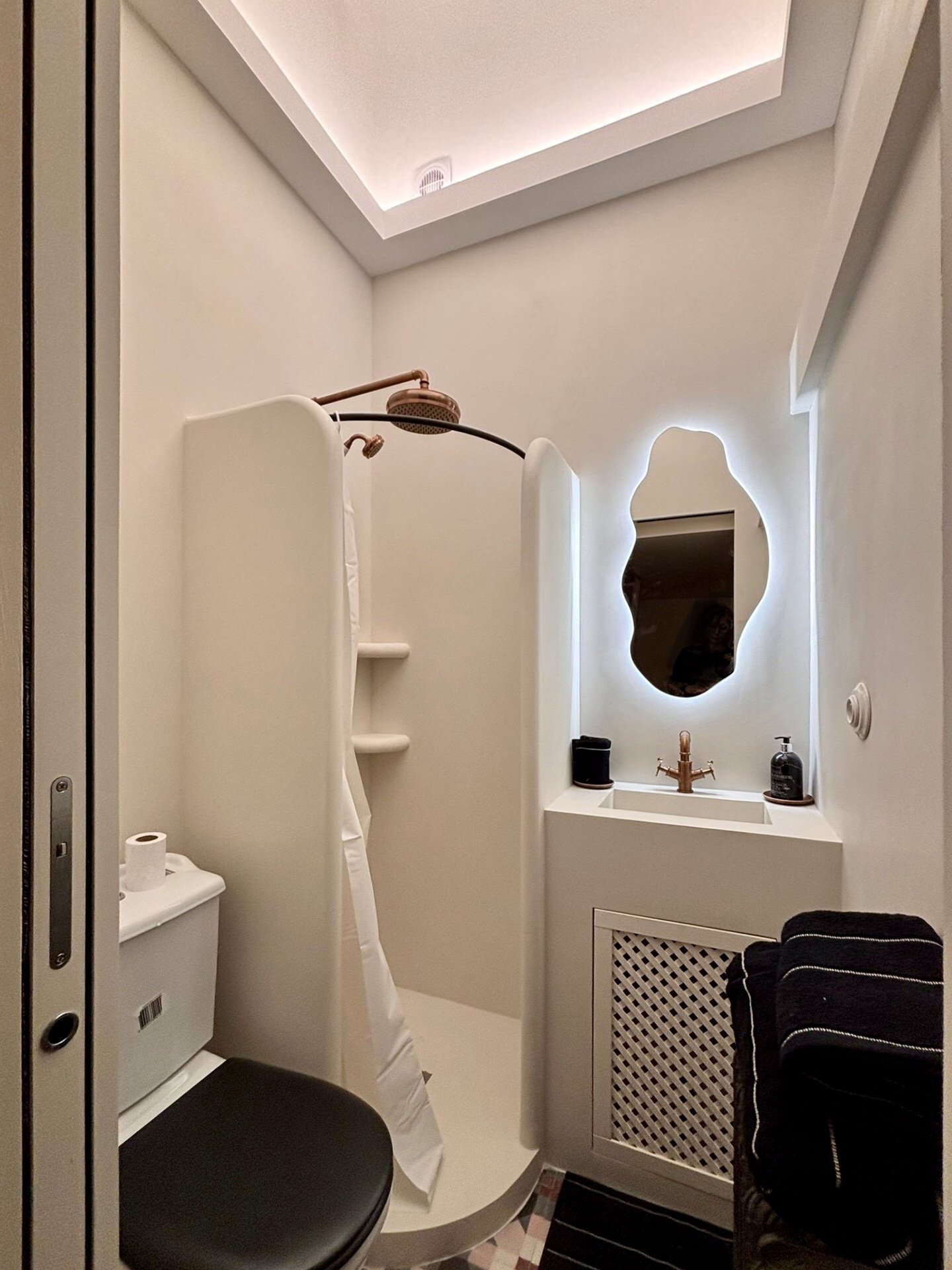 Petite salle de bain moderne avec lavabo, miroir avec éclairage, espace douche avec paroi, toilettte, et meubles de rangement.