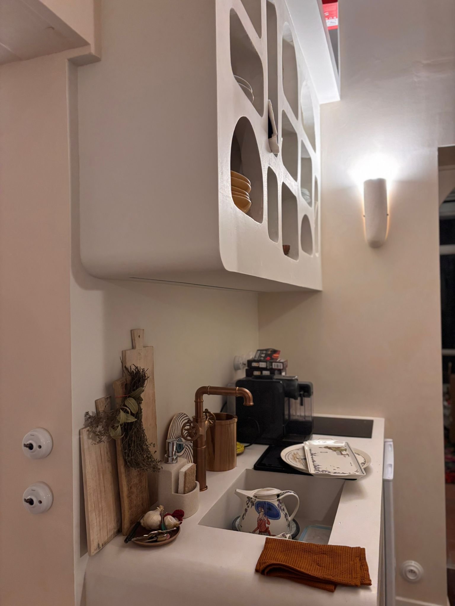 Cuisine avec plan de travail montrant des ustensiles, un porte-savon en cuivre, un colander, un livre de cuisine ouvert, et une tasse avec une illustration.