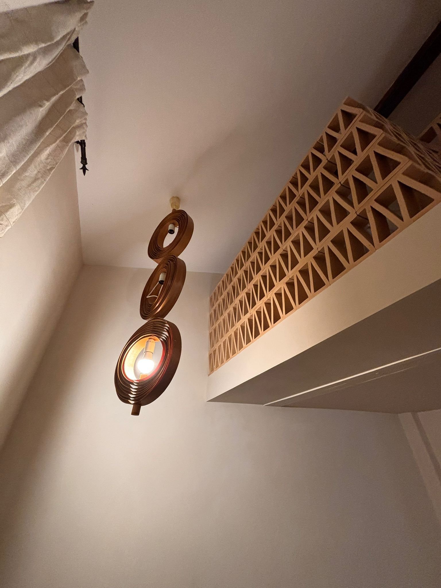 Lampes design en bois suspendues au plafond dans une pièce avec un mur beige clair et une réserve à vin en bois.