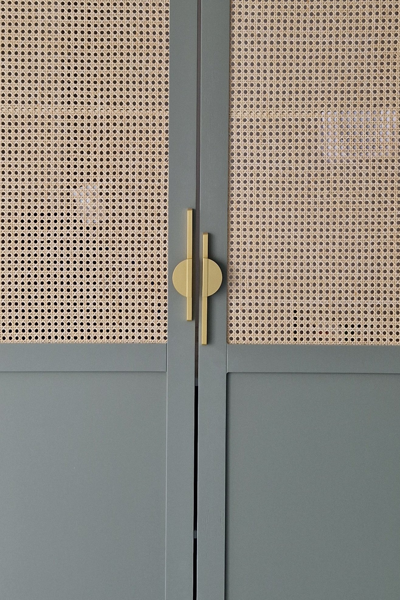 Une porte double couleur gris avec des poignées en forme de cercle dorées. La partie supérieure de chaque porte est en matériau en treillis en bois, laissant passer la lumière.