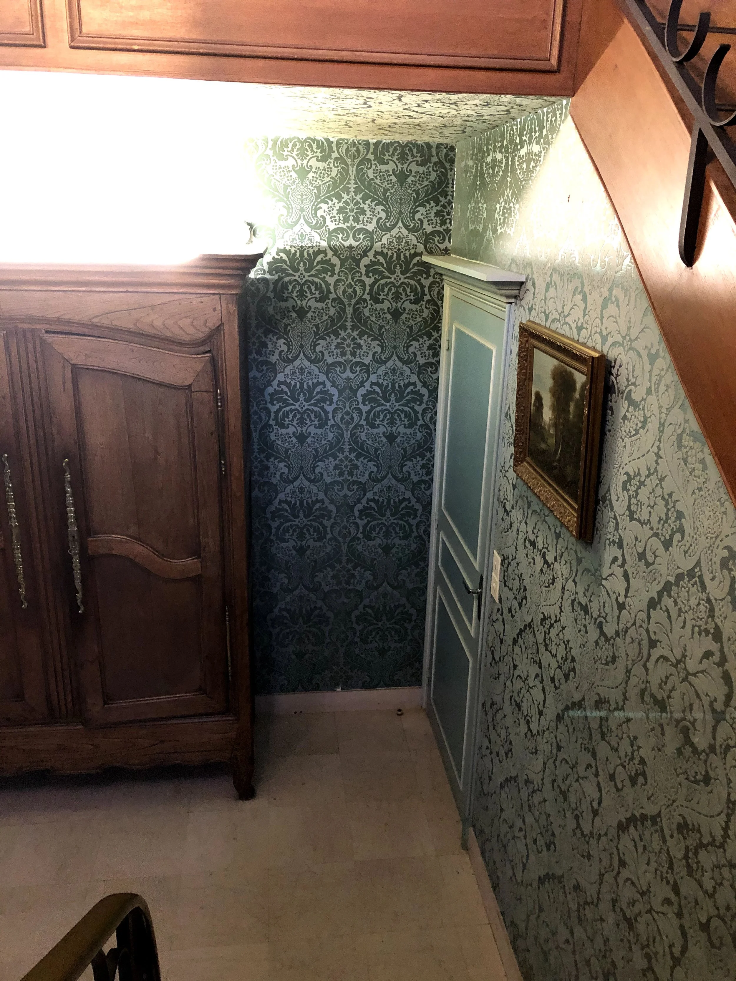 Un coin de pièce avec un mur décoratif à motifs, une armoire en bois, une porte blanche, un tableau encadré et un tapis.