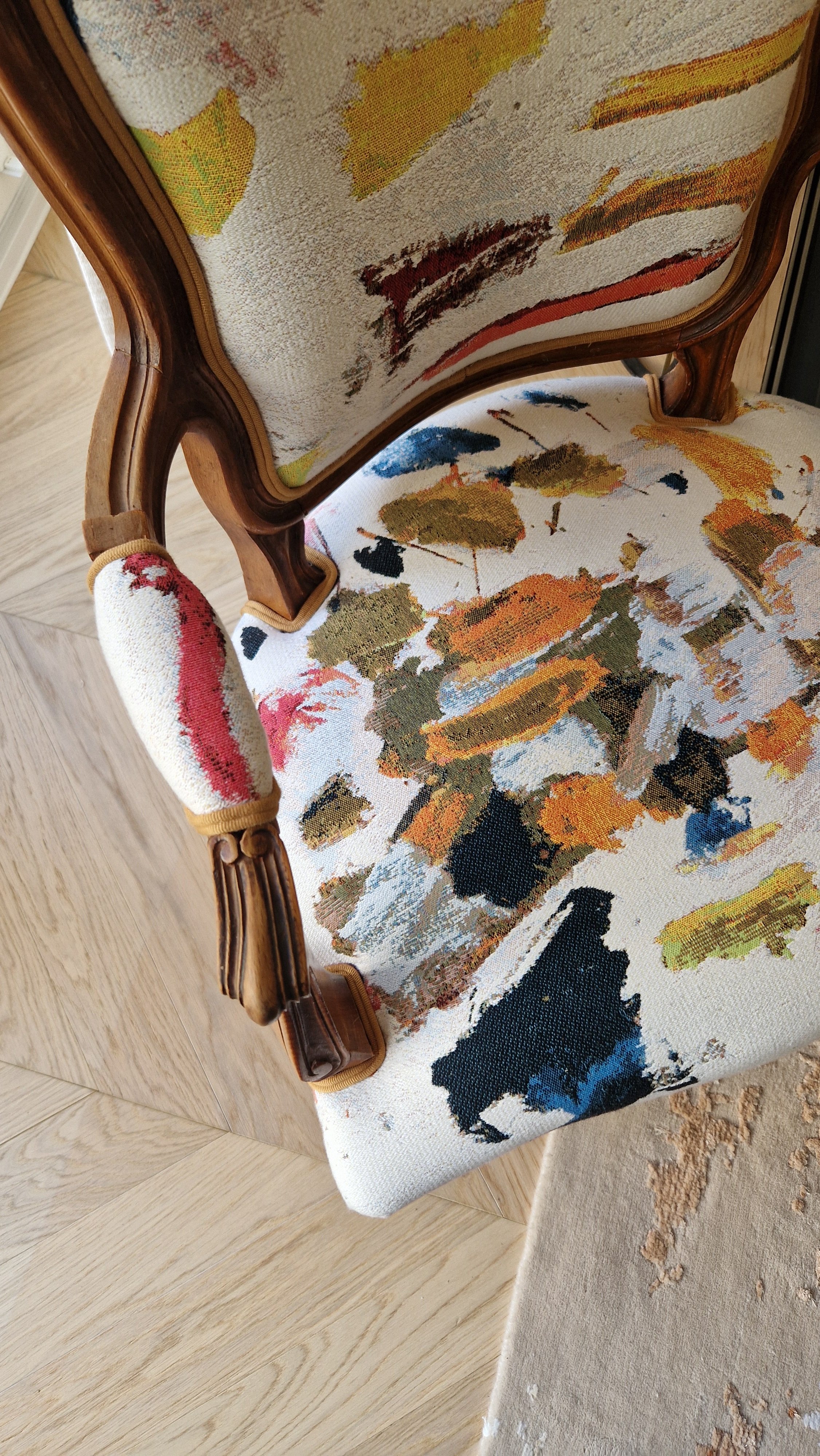 Chaise ancienne avec un tissu à motifs abstraits colorés en jaune, vert, orange, bleu et noir, avec une structure en bois.