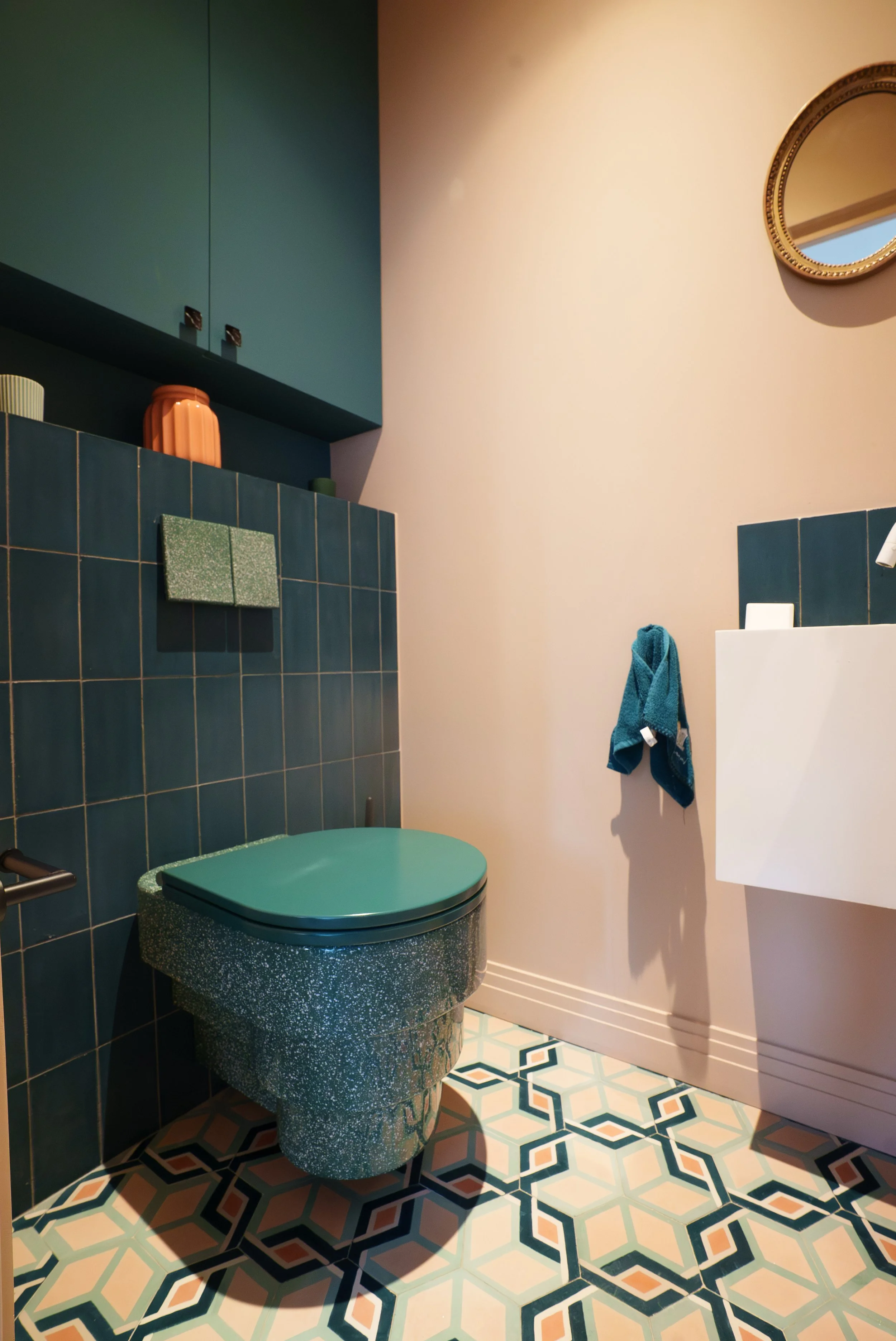 Salle de bain moderne avec carrelage bleu et motifs géométriques, toilette de style vintage avec couleur verte, miroir rond doré, serviette bleue accrochée, porte blanche