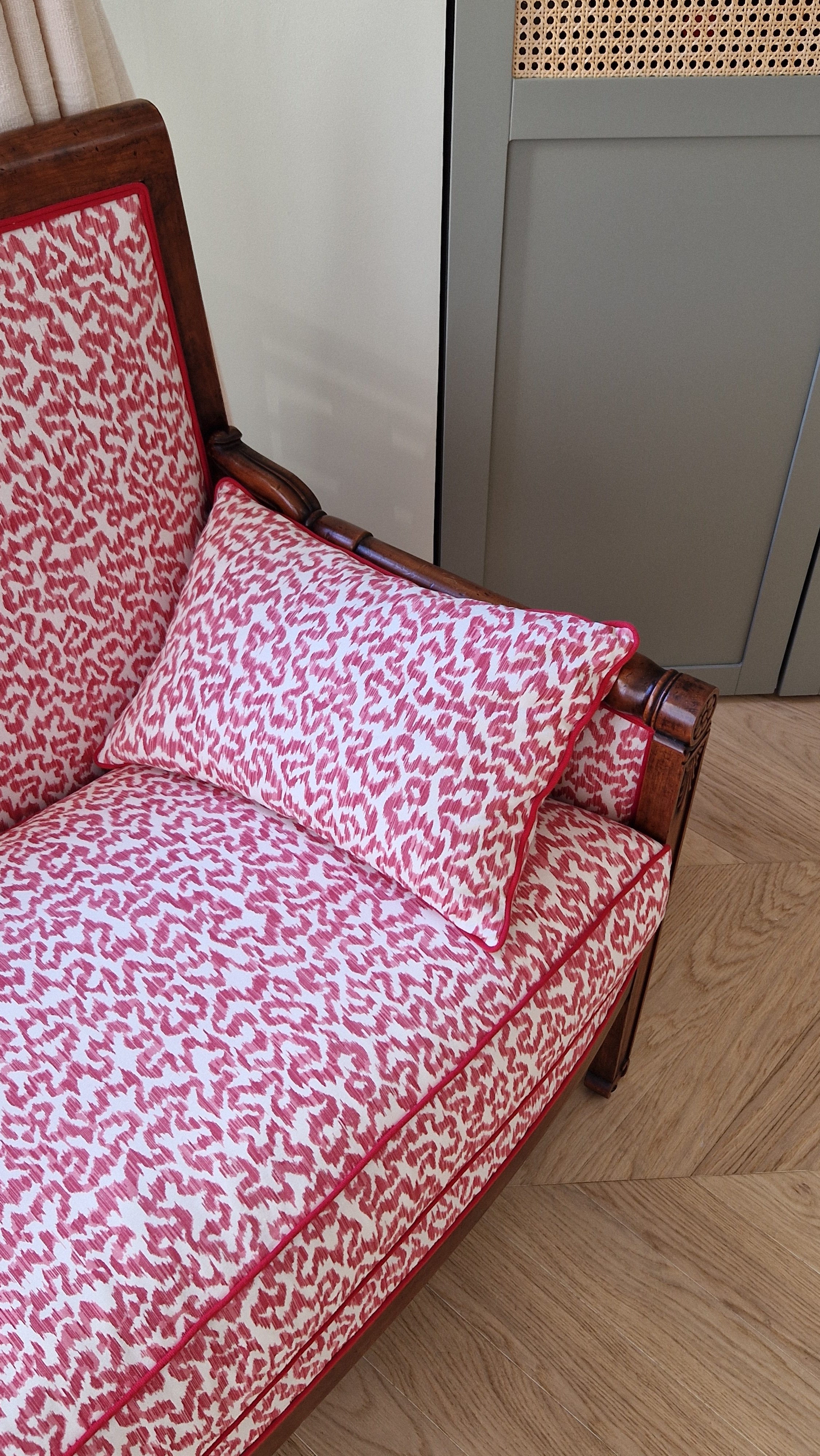 Un canapé en bois avec un revêtement en tissu rose et blanc à motif abstrait, une repose-tête en coussin assorti, dans une pièce avec mobilier en bois et un sol en parquet.