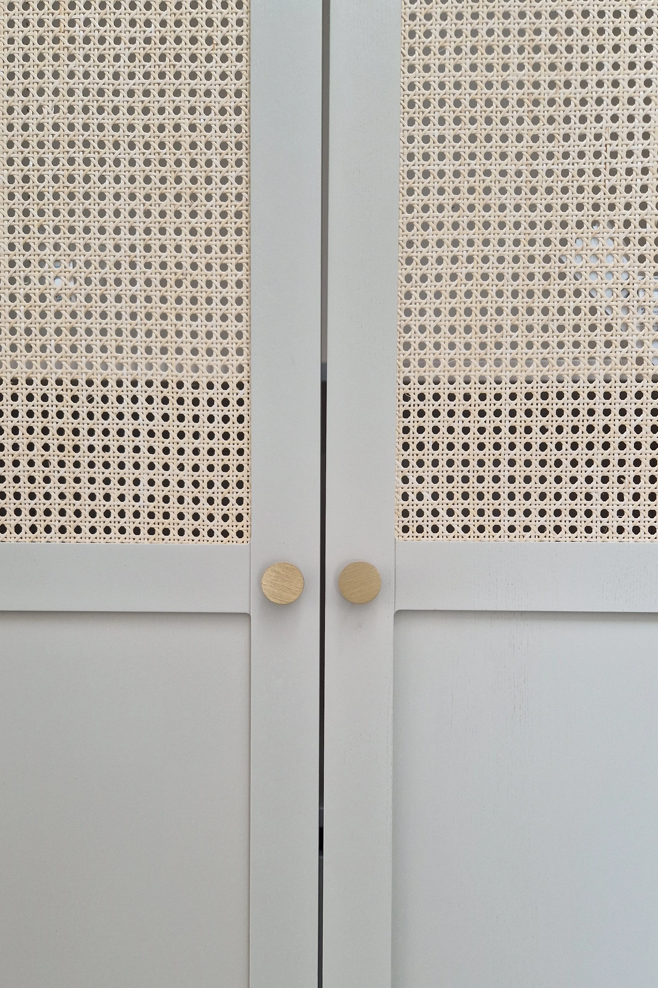 Une porte blanche avec des panneaux en rotin et deux poignées rondes en bois.