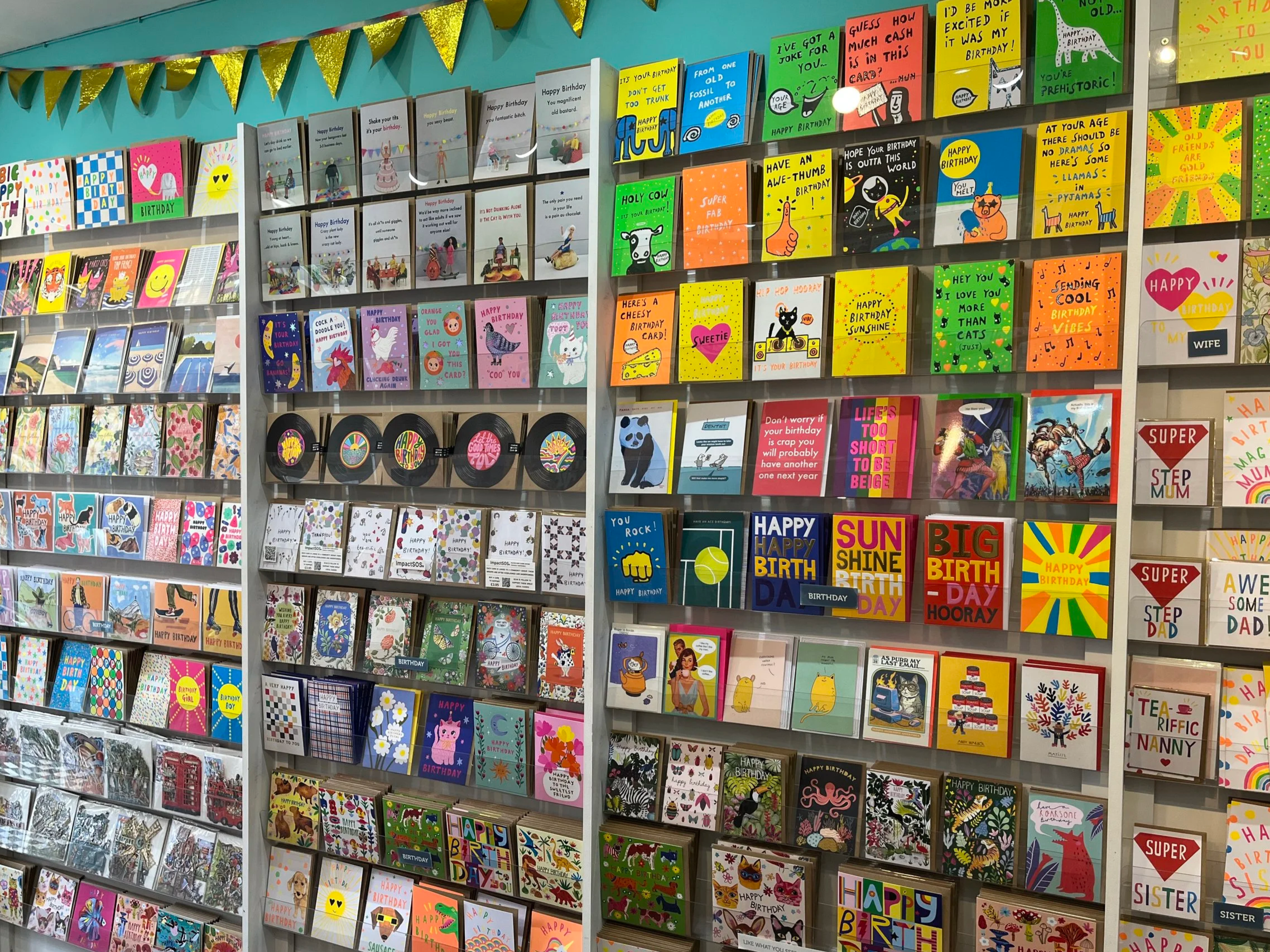Multiple shelves filled with colourful birthday greeting cards, organized in rows with various designs, illustrations, and messages.