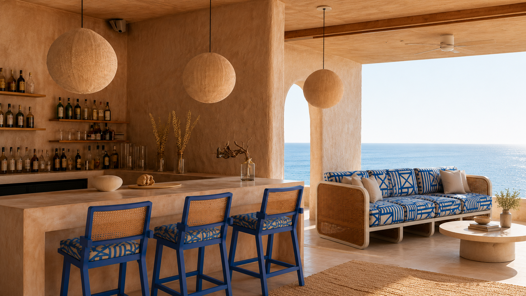 Beachfront living room with bar area, beige walls, wooden ceiling, hanging woven pendant lights, blue patterned sofa with white cushions, round coffee table, ocean view, and minimal decor.