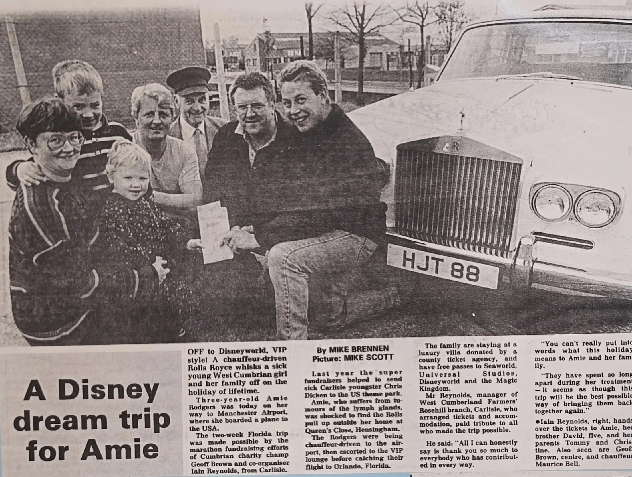 Black and white newspaper photo showing a group of seven people, including children and adults, gathered outdoors next to a vintage Rolls Royce car. The scene appears to be related to a charity event or holiday trip, with some individuals smiling and