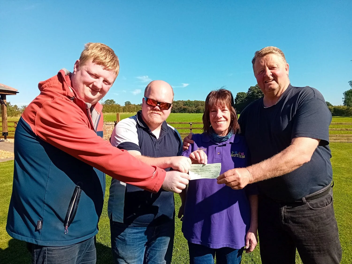 Group of four people outdoors on a sunny day holding a check.