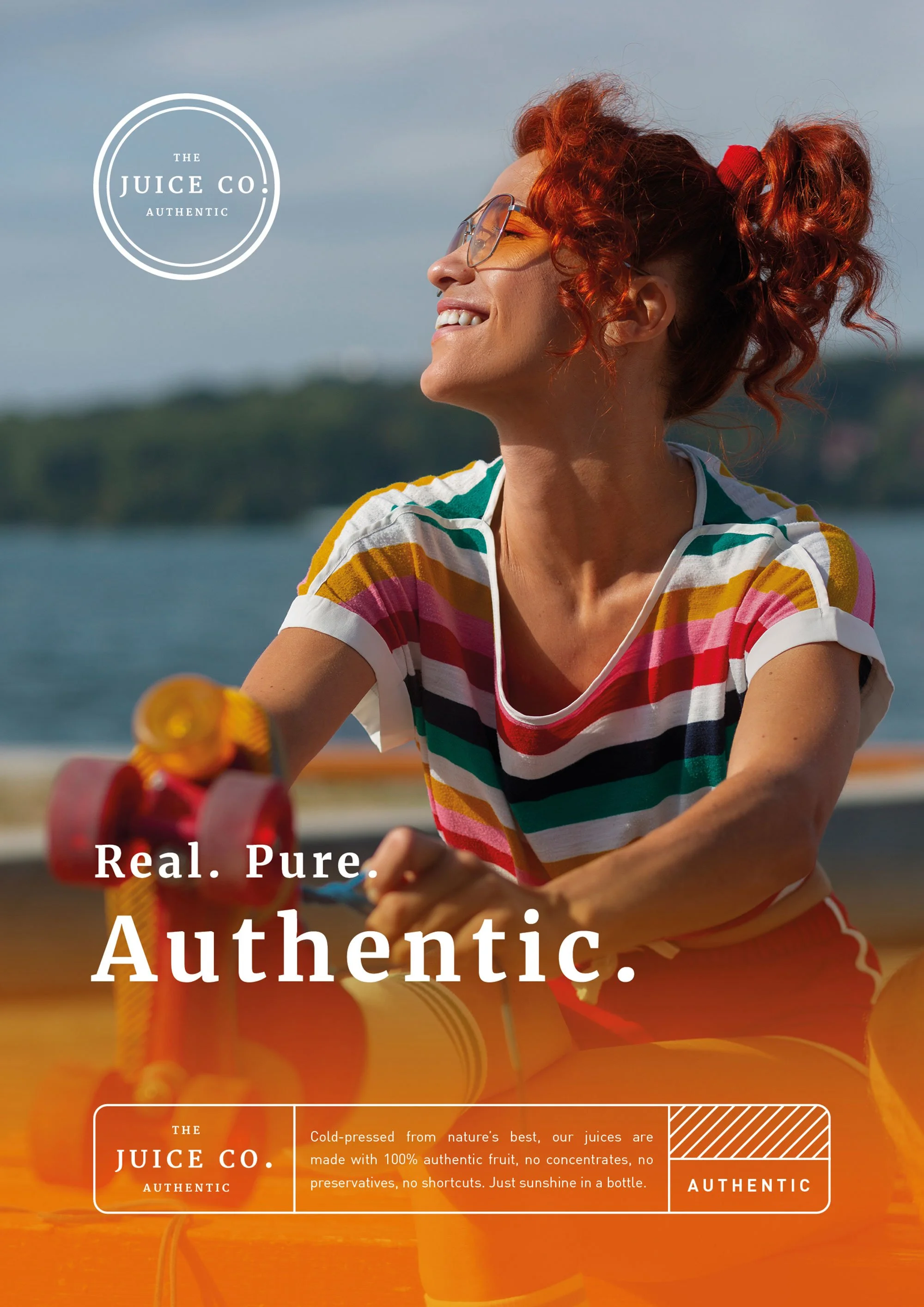 A woman with curly red hair and yellow-tinted glasses smiling outdoors near a body of water, wearing a colorful striped shirt, with a logo for 'The Juice Co. Authentic' overlayed on the image, and additional text about the product.